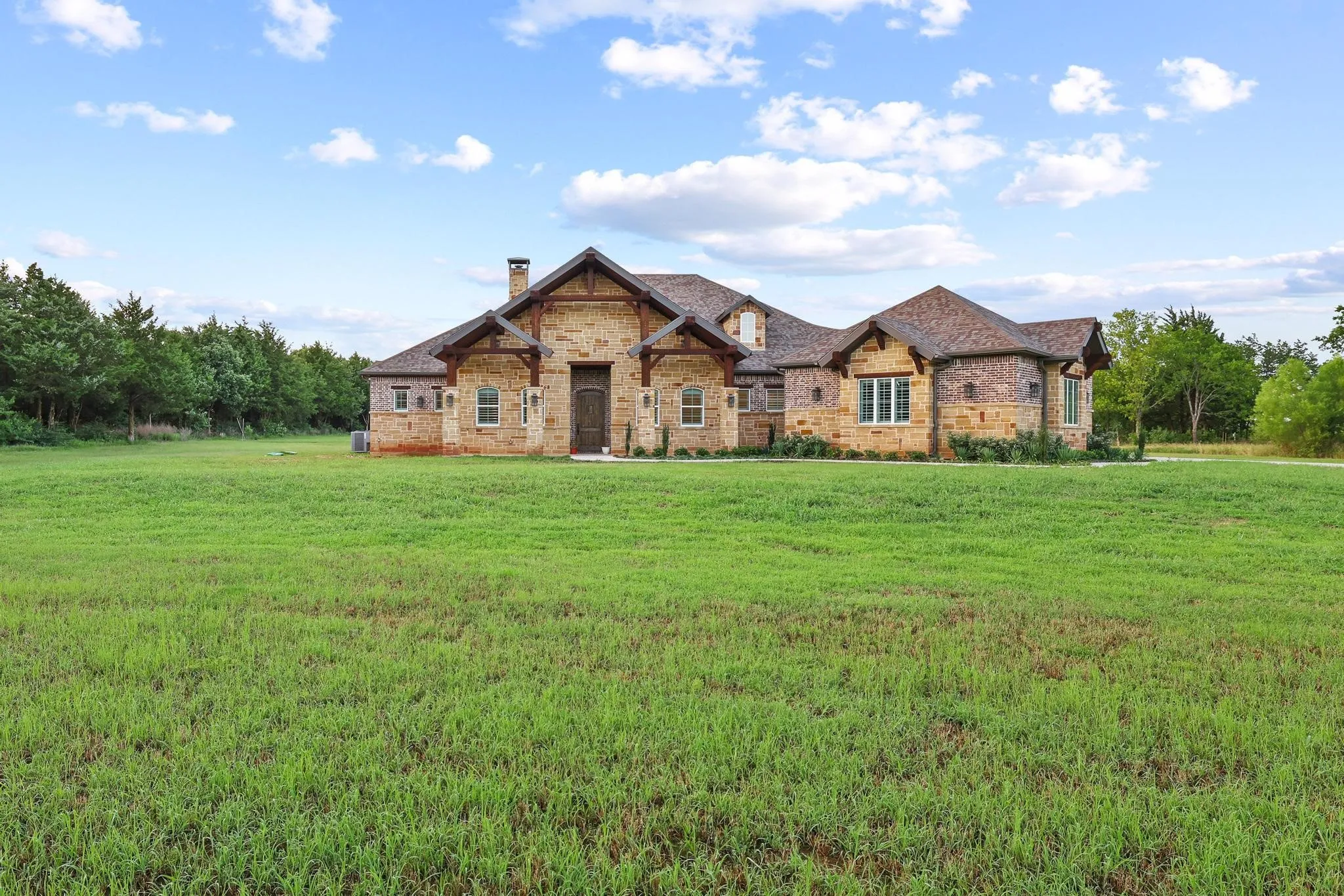 Stone and brick facade home featuring a prominent front entrance with a dark wood door, a gabled roofline with dark shingles, and multiple windows with white trim