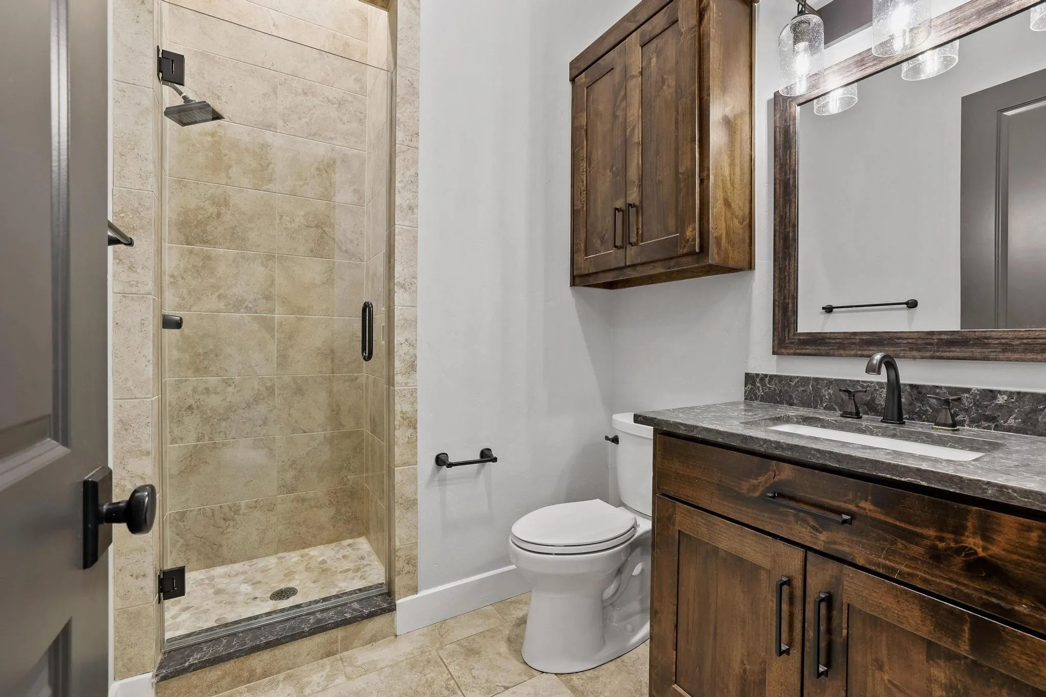 Bathroom featuring a glass-enclosed shower with tile surround, dark wood vanity with undermount sink, dark stone countertop, and dark wood-framed mirror
