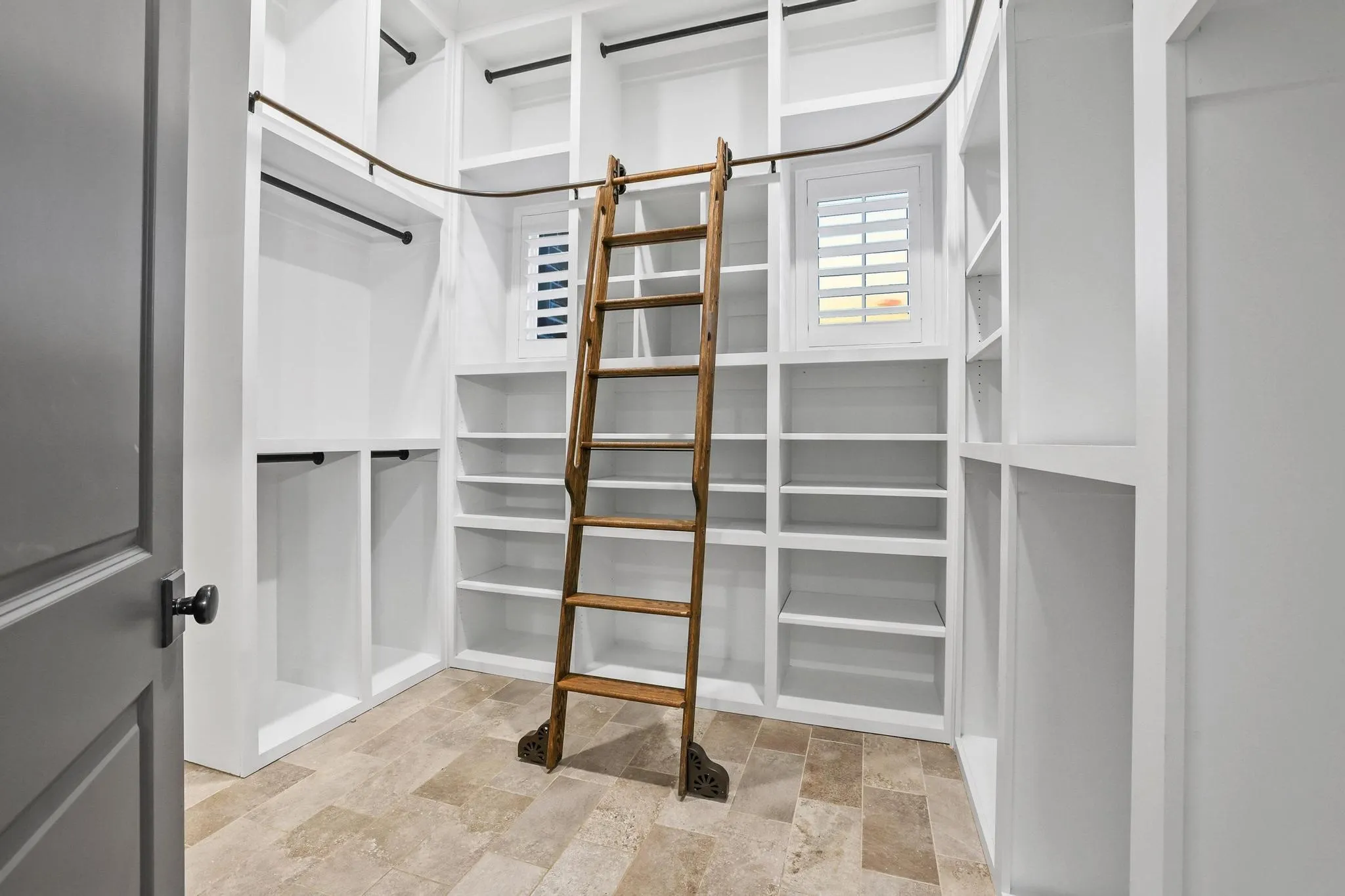 Custom storage room featuring extensive white built-in shelving, multiple hanging rods, and a rolling wooden ladder