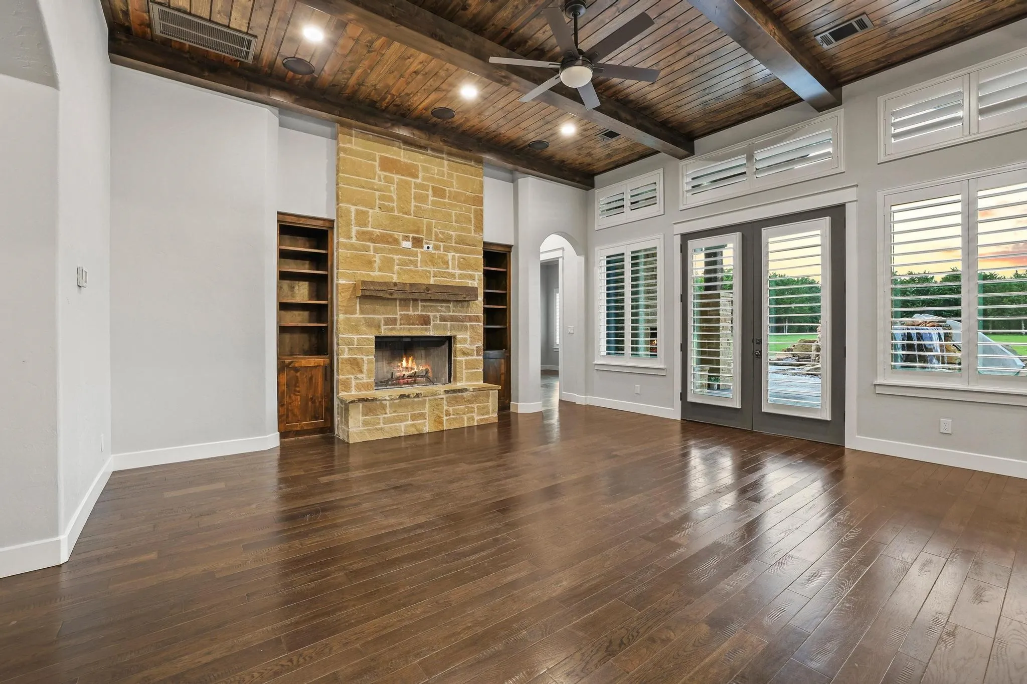 Spacious living area featuring wood-finish flooring, a stone fireplace with a wood mantel, and built-in shelving
