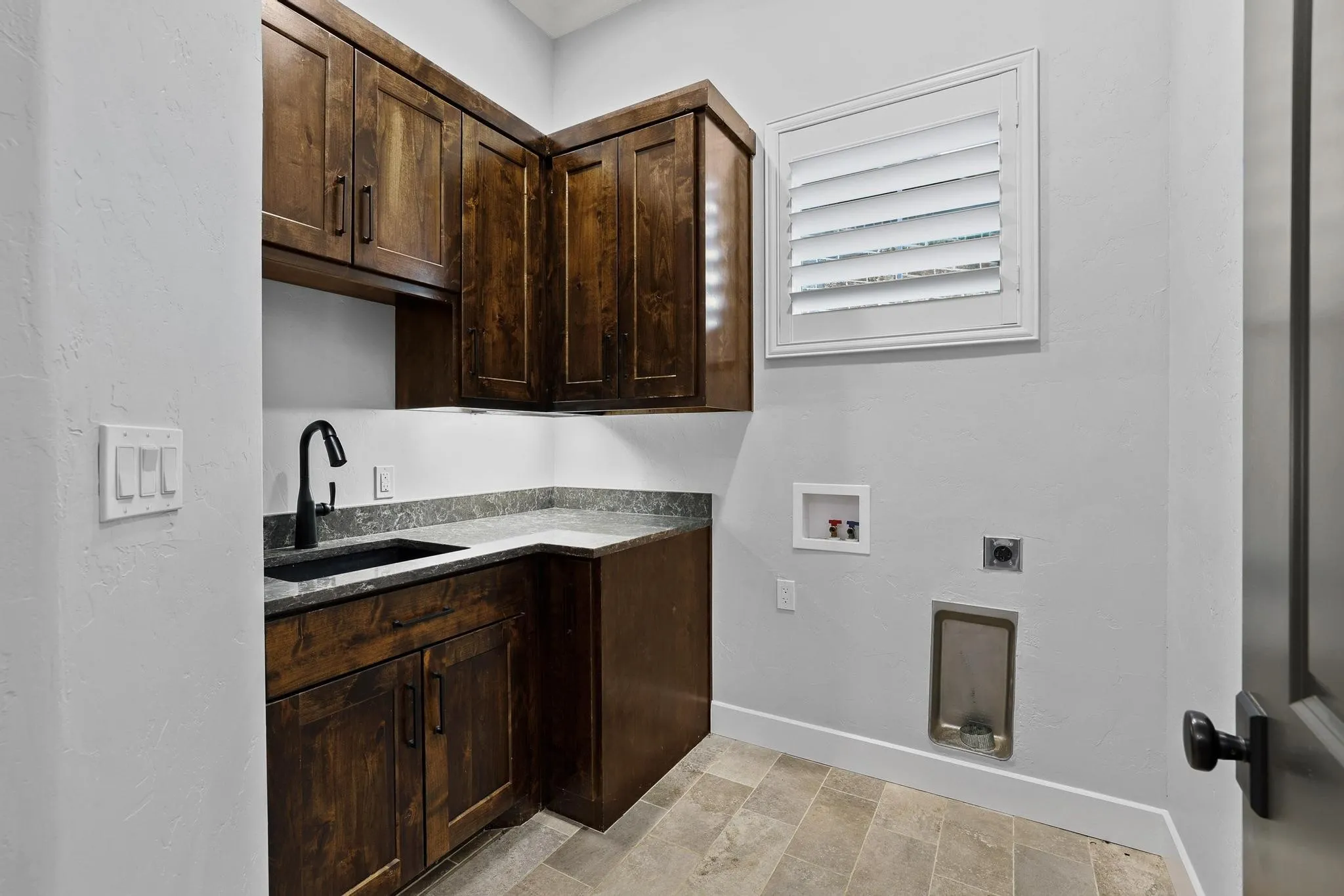 Dedicated utility space featuring dark wood cabinetry, a built-in sink with a matte black faucet, and stone-finish countertops