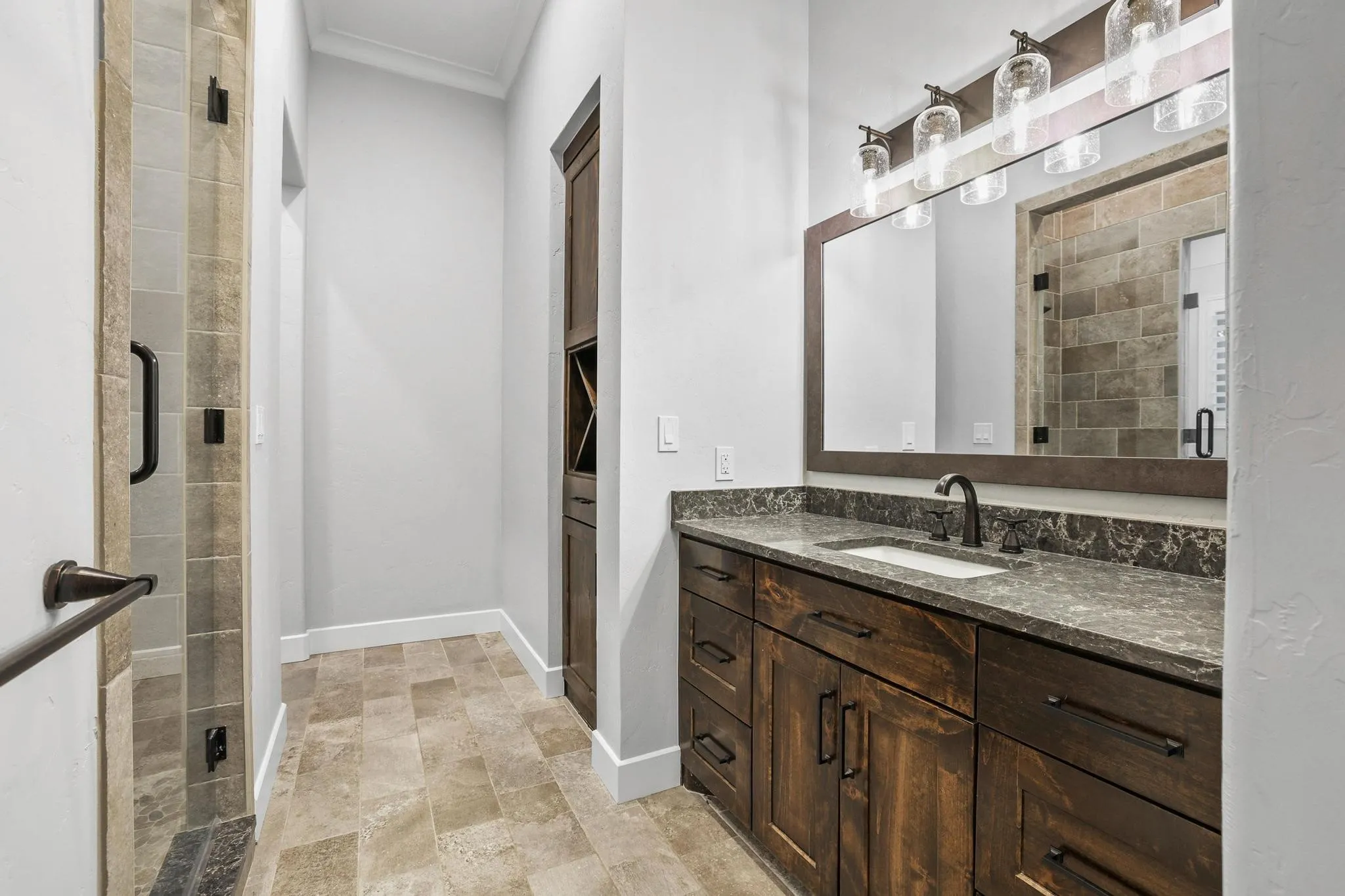 Spacious bathroom featuring a wood-finish vanity with a dark stone countertop, an undermount sink, and a bronze-finish faucet