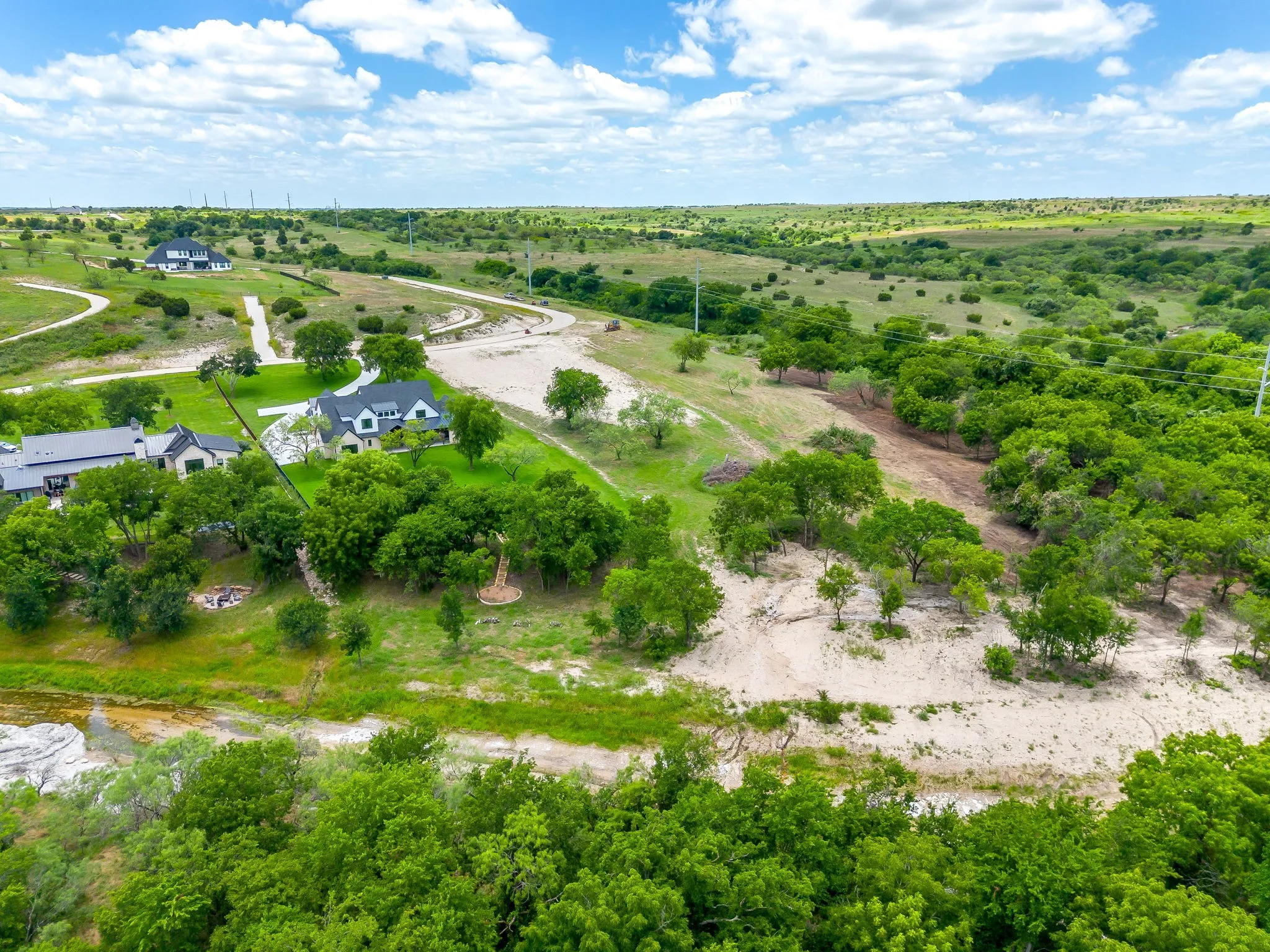 Extensive property featuring a primary residence with a dark roof and light exterior, surrounded by mature trees and natural landscaping