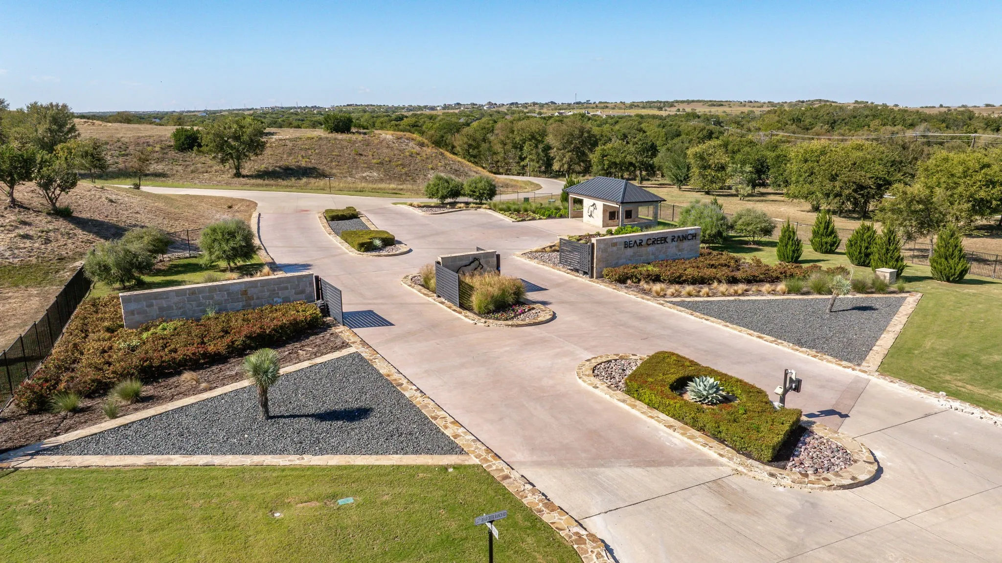 Main entrance featuring a stone perimeter wall, concrete driveway, and a guardhouse