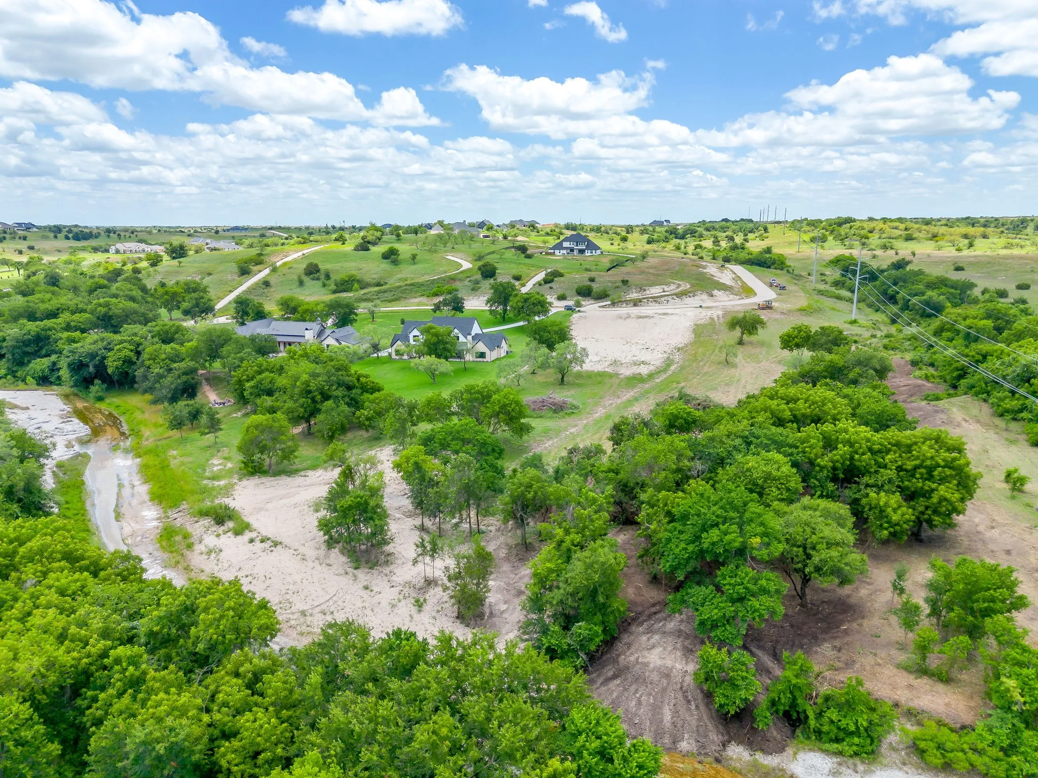 Expansive rural property featuring a winding driveway, scattered mature trees, and a partially developed landscape