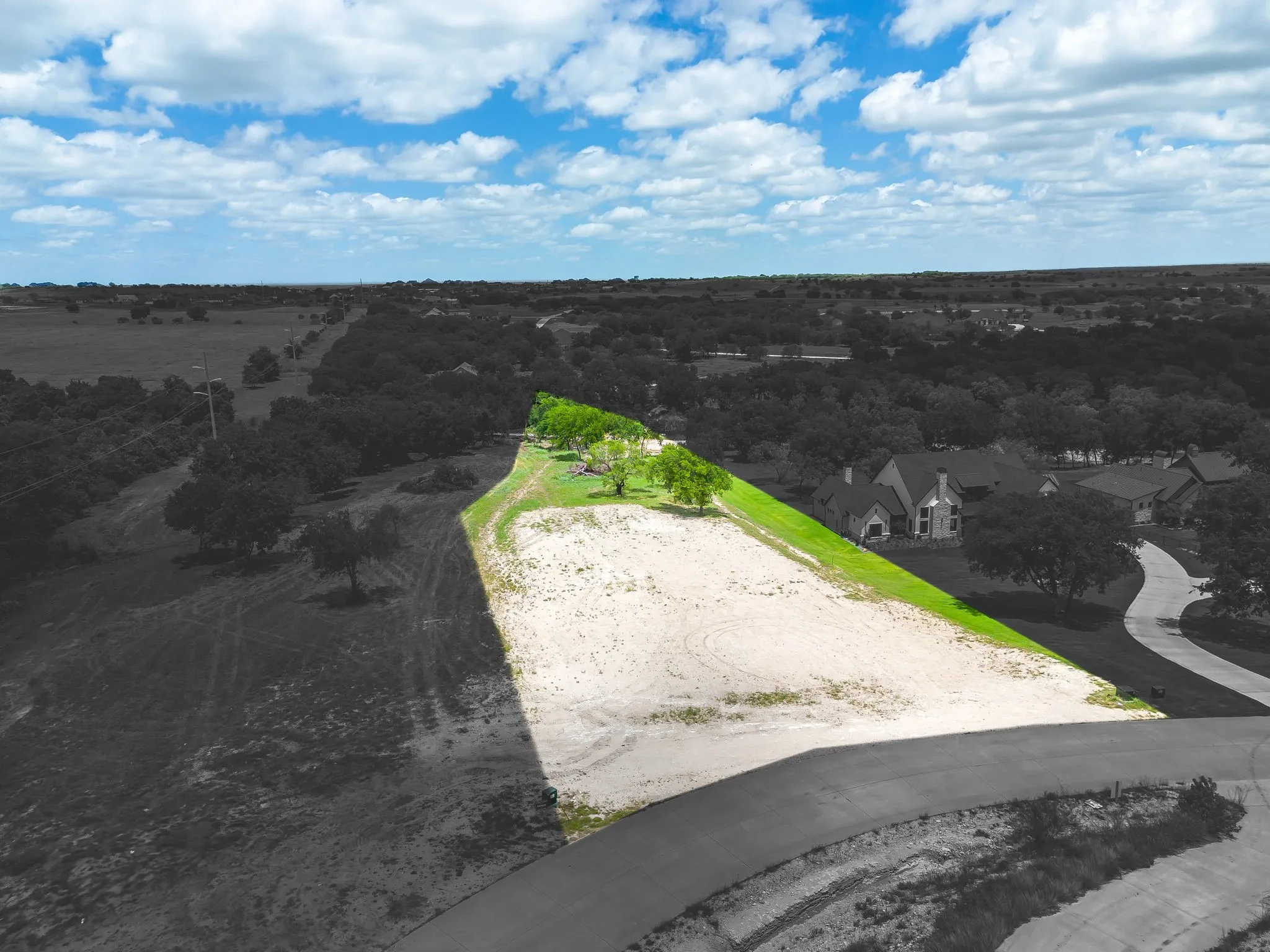 Expansive undeveloped lot featuring a sloped terrain, scattered mature trees, and direct road frontage