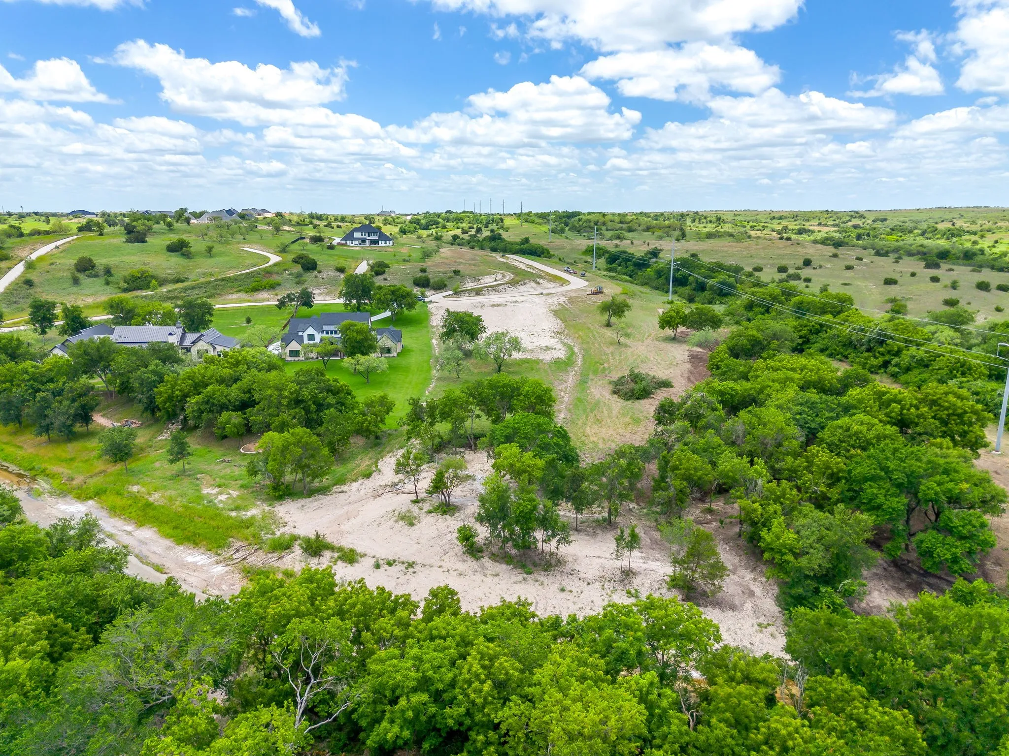 Expansive undeveloped land featuring natural topography, mature trees, and existing residential structures in the distance