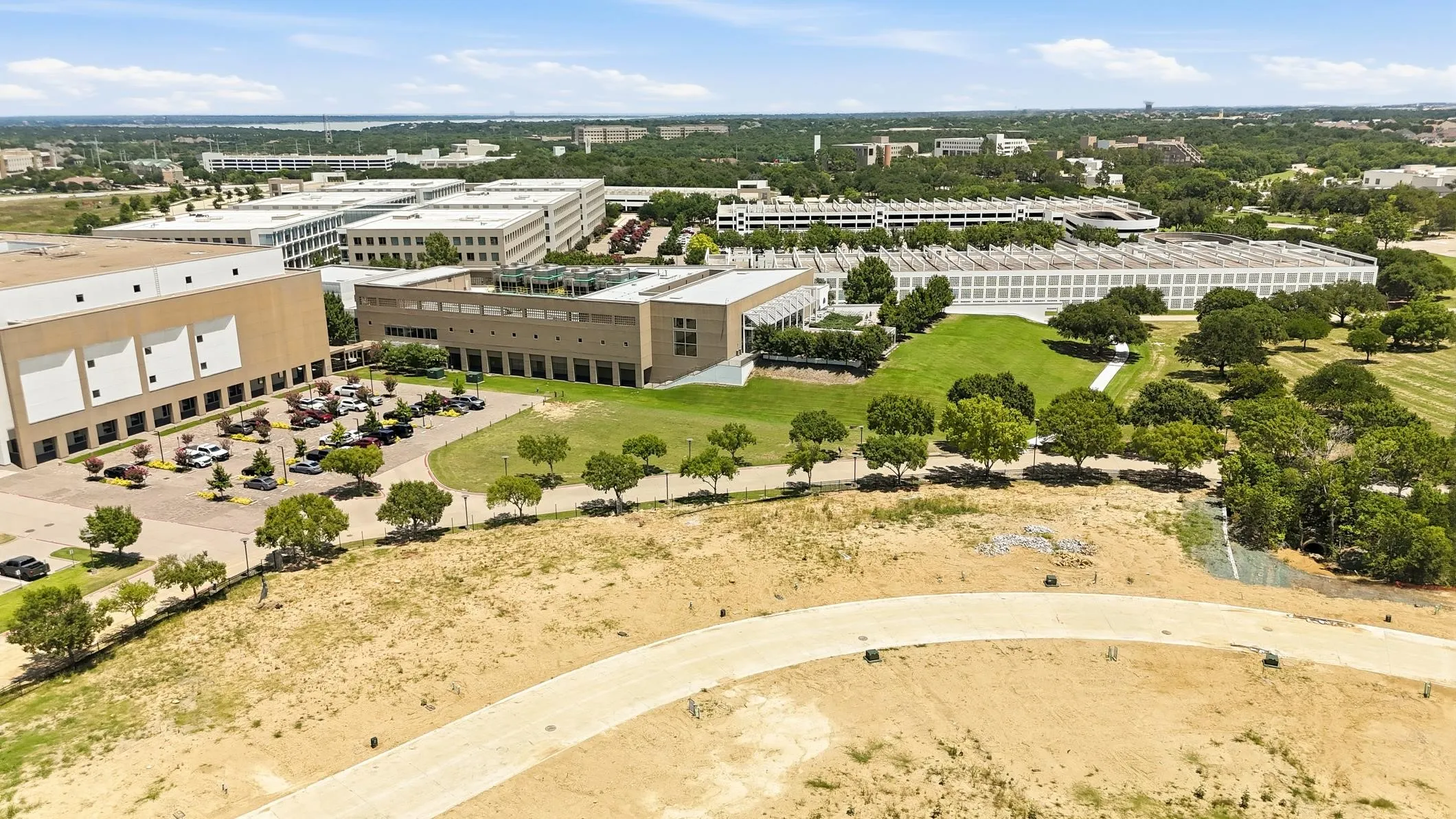 Expansive commercial property featuring multiple modern buildings with extensive parking, manicured green spaces, and mature tree landscaping
