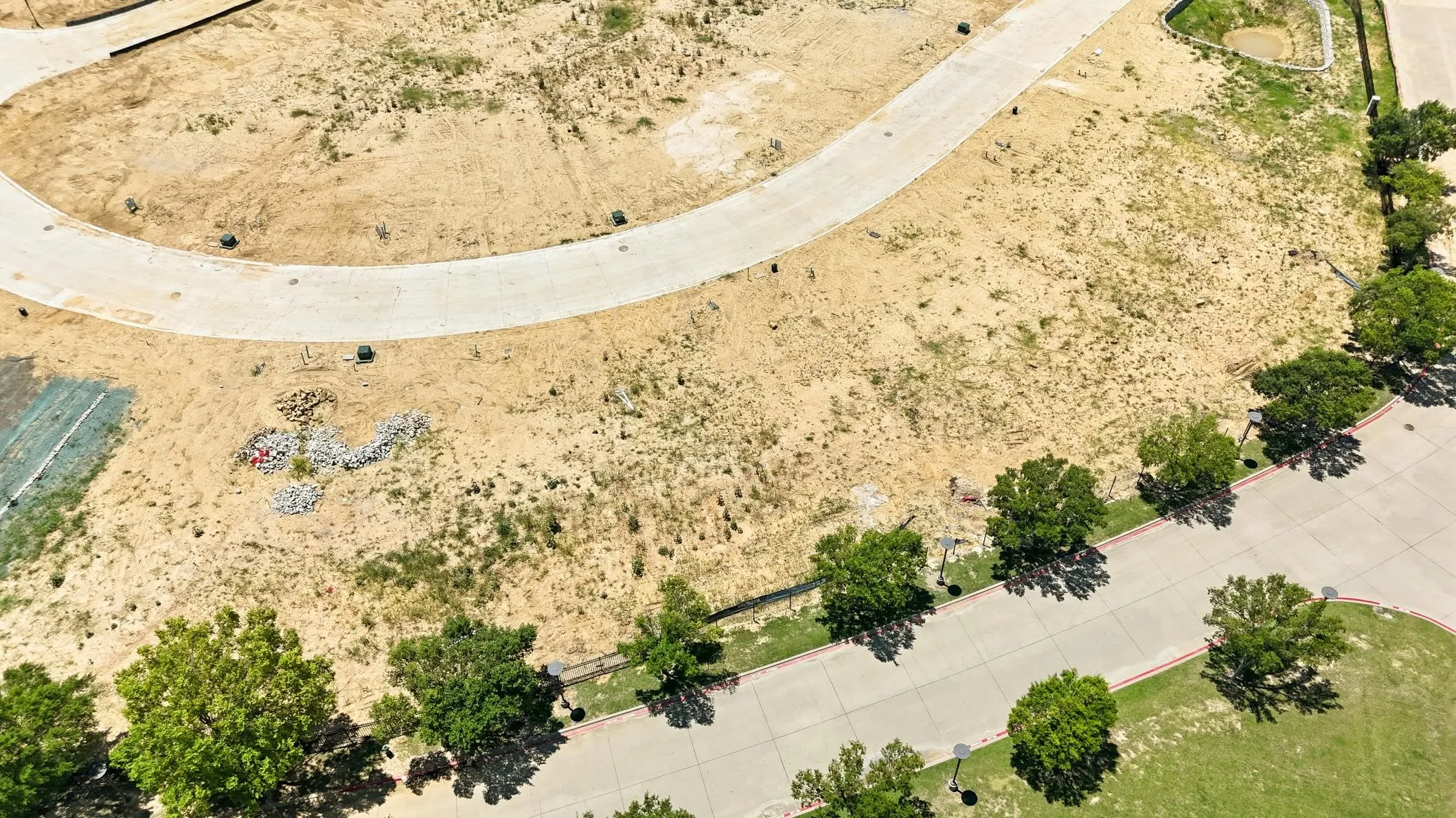 Expansive undeveloped parcel featuring a curved concrete pathway, surrounding natural terrain, and mature trees lining a paved street