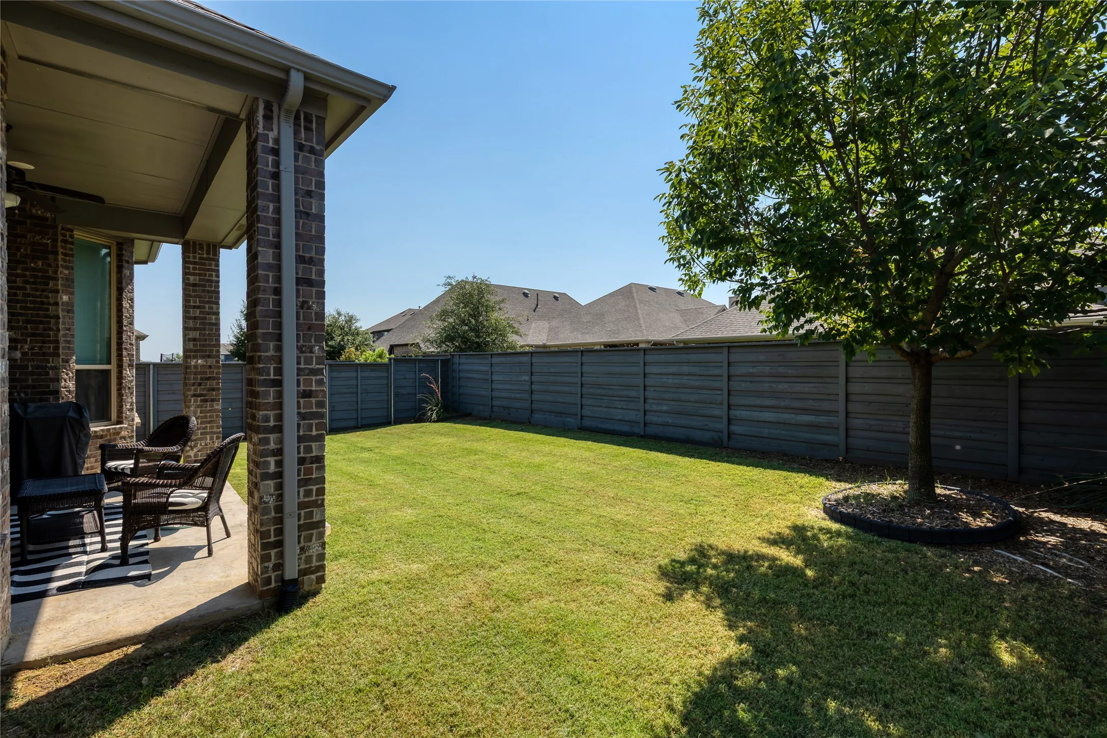 Expansive backyard featuring a manicured lawn, a mature shade tree with a defined tree ring, and a durable horizontal plank fence