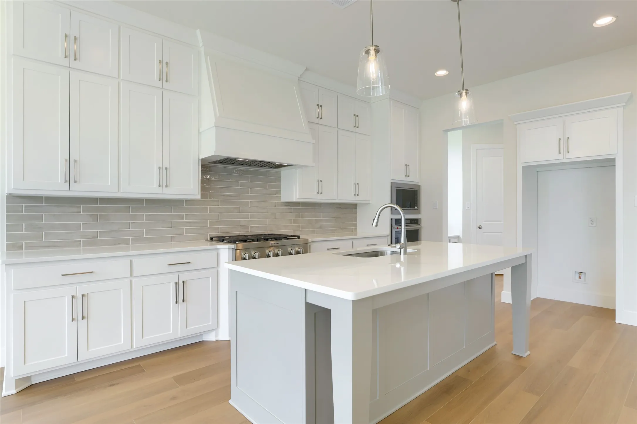 Gourmet kitchen featuring white shaker cabinetry, light wood-finish flooring, and a large center island with a sink
