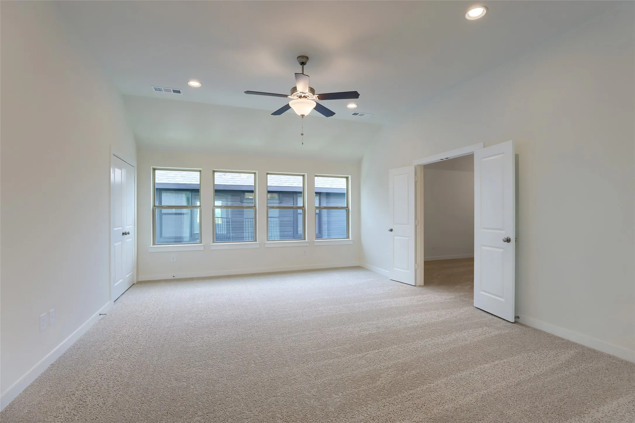 Spacious room with plush carpeting, three large windows, a ceiling fan with light fixture, recessed lighting, and double entry doors