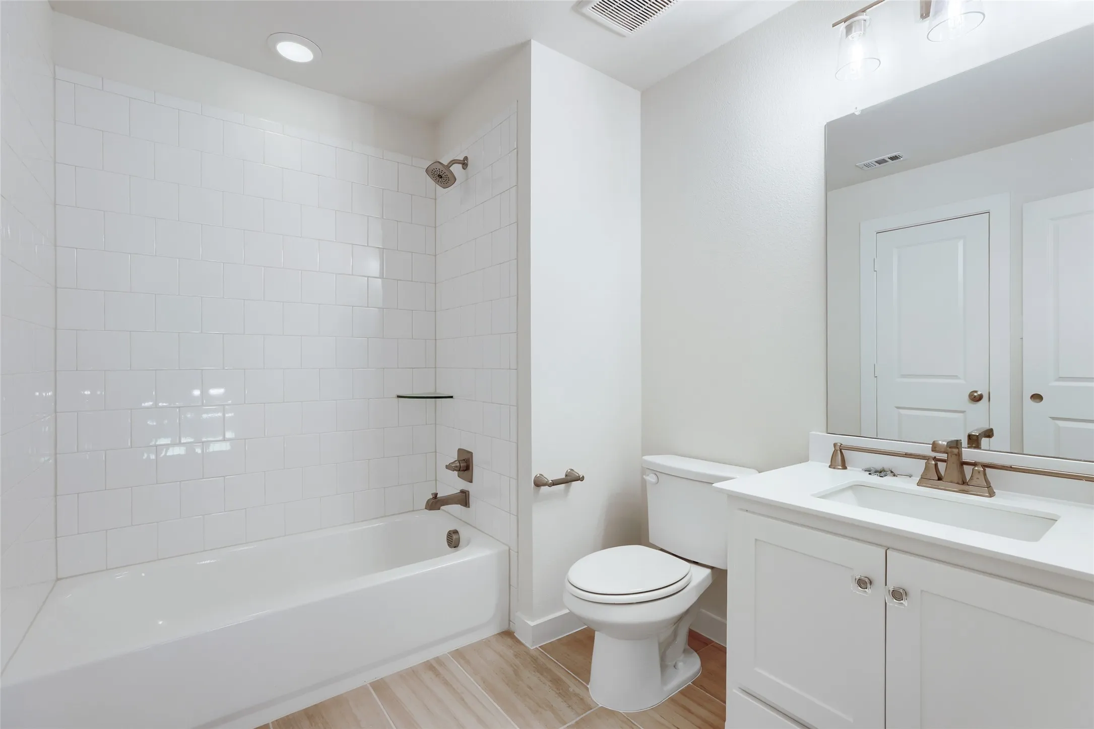 Bathroom featuring a white subway tile tub surround, bronze-finish fixtures, single vanity with white cabinetry, a rectangular mirror, and wood-look flooring