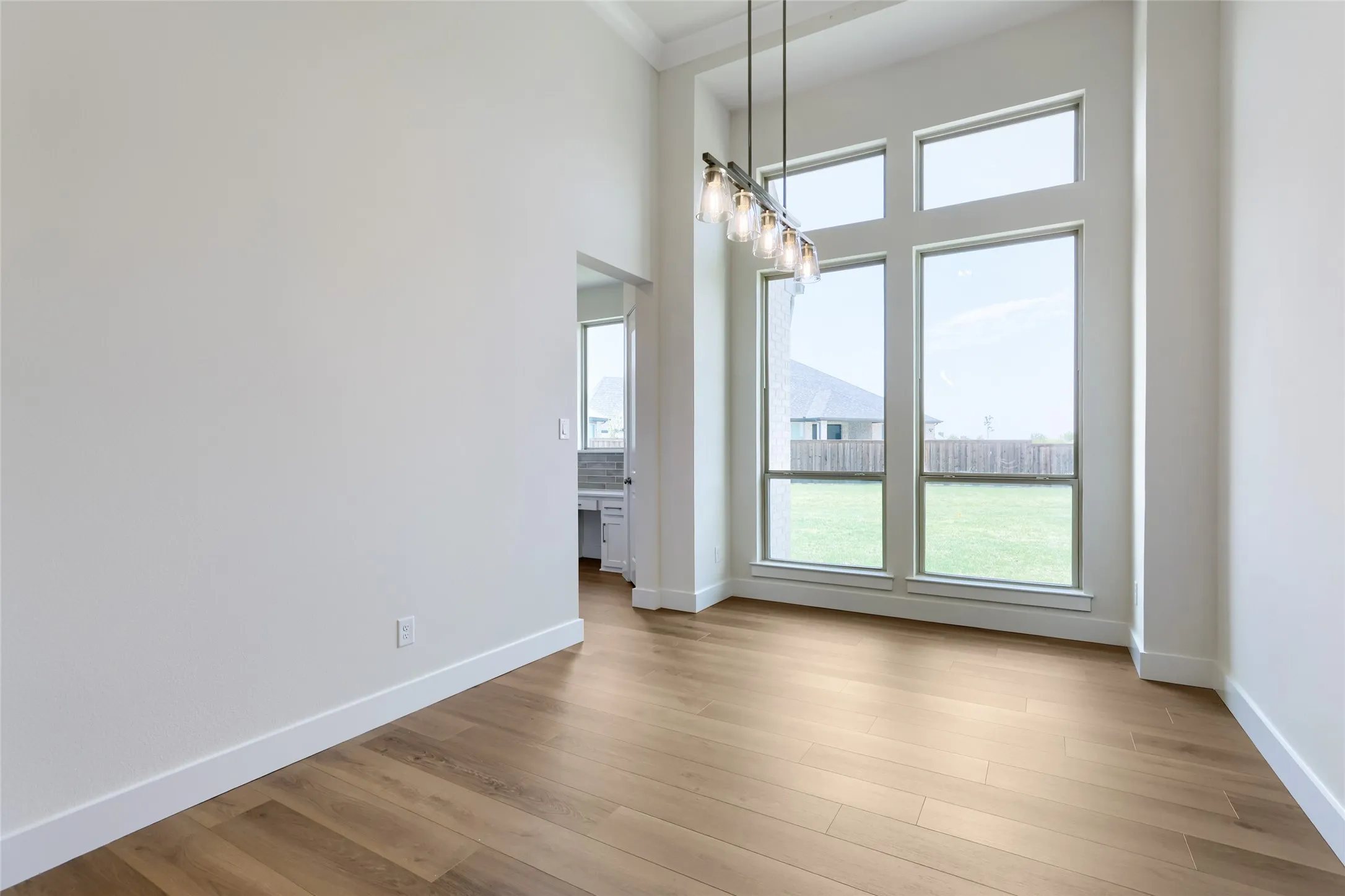 Two-story windows illuminating a spacious interior with wood-finish flooring, a tiered linear chandelier, and a recessed ceiling