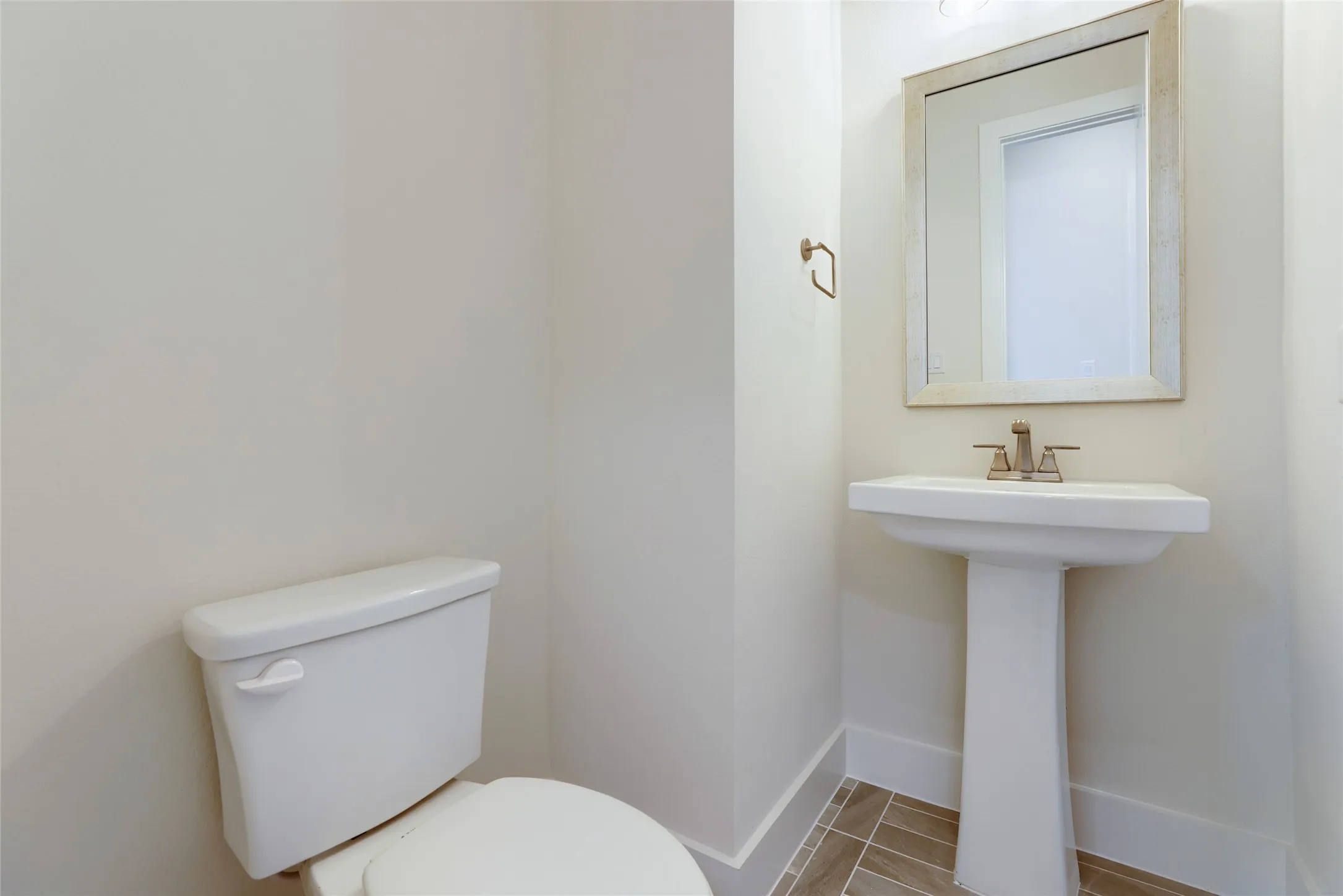 Pedestal sink with a framed mirror, brushed nickel faucet, and tile flooring