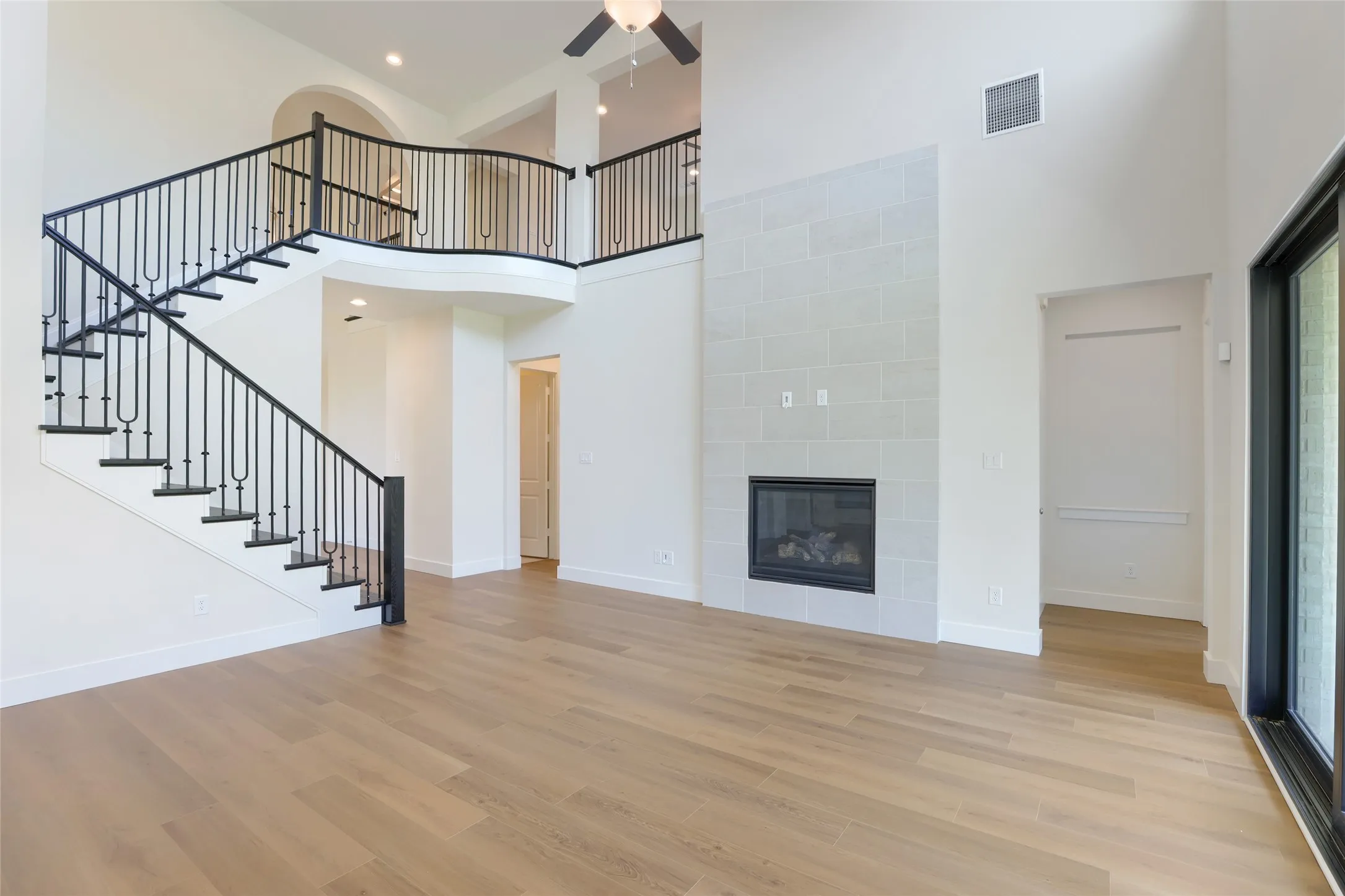 Two-story living area featuring wood-finish flooring, a contemporary fireplace with a tiled surround, and a sweeping staircase with black wrought iron balusters