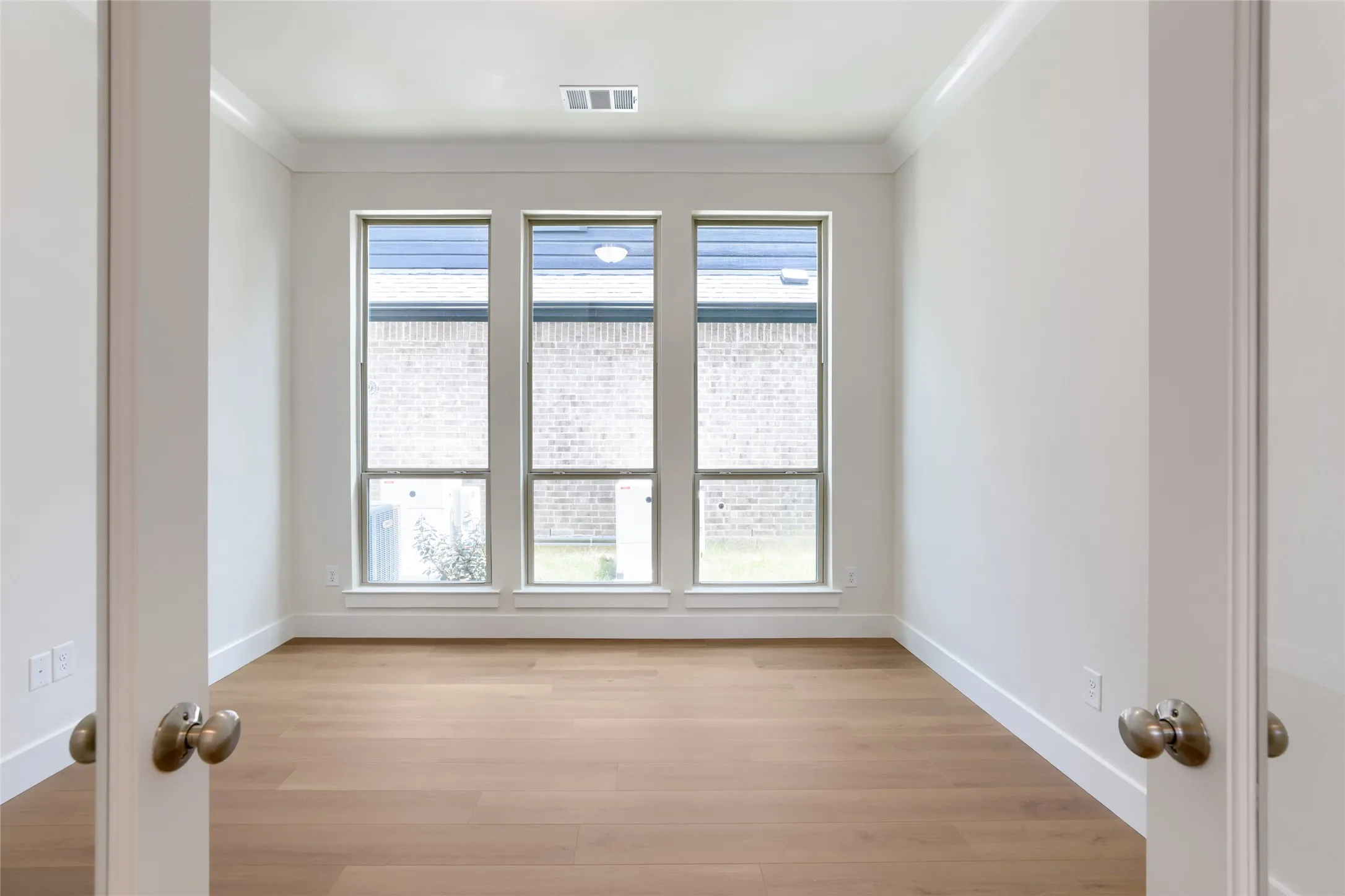 Room featuring wood-finish flooring, white walls, and a trio of tall windows