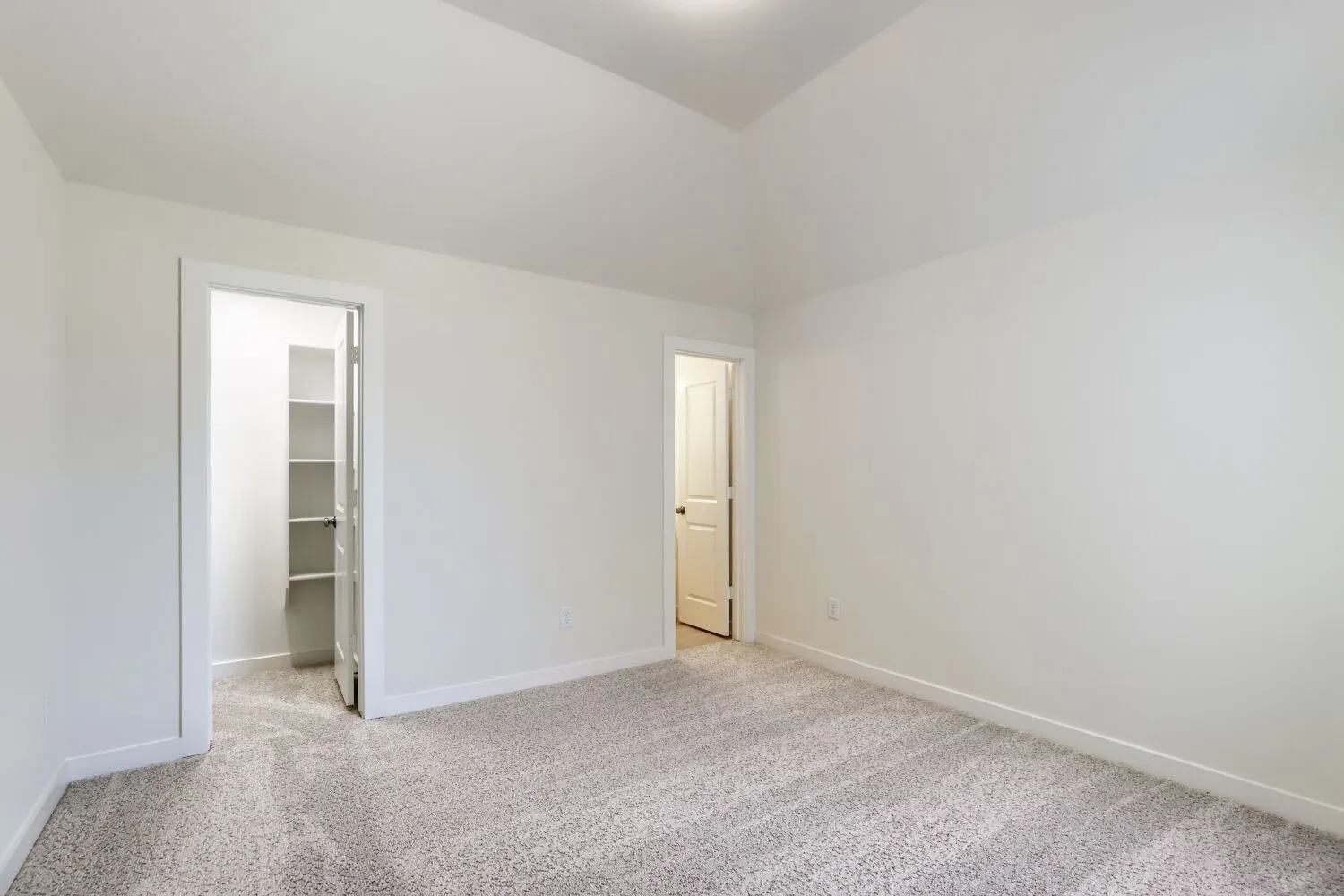 Spacious room featuring vaulted ceilings, light gray carpeting, crisp white walls, and bright white trim