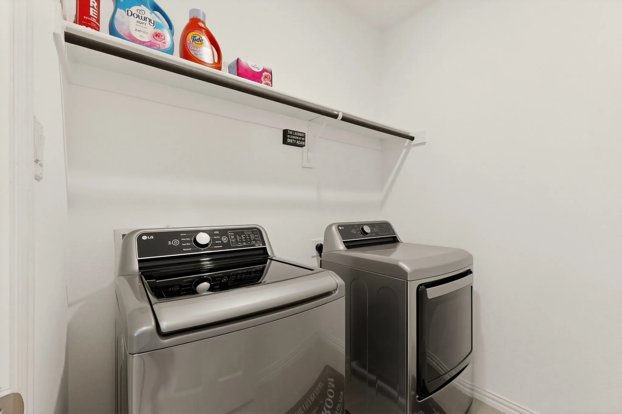 A bright utility room with a washer, a dryer, and a shelf overhead
