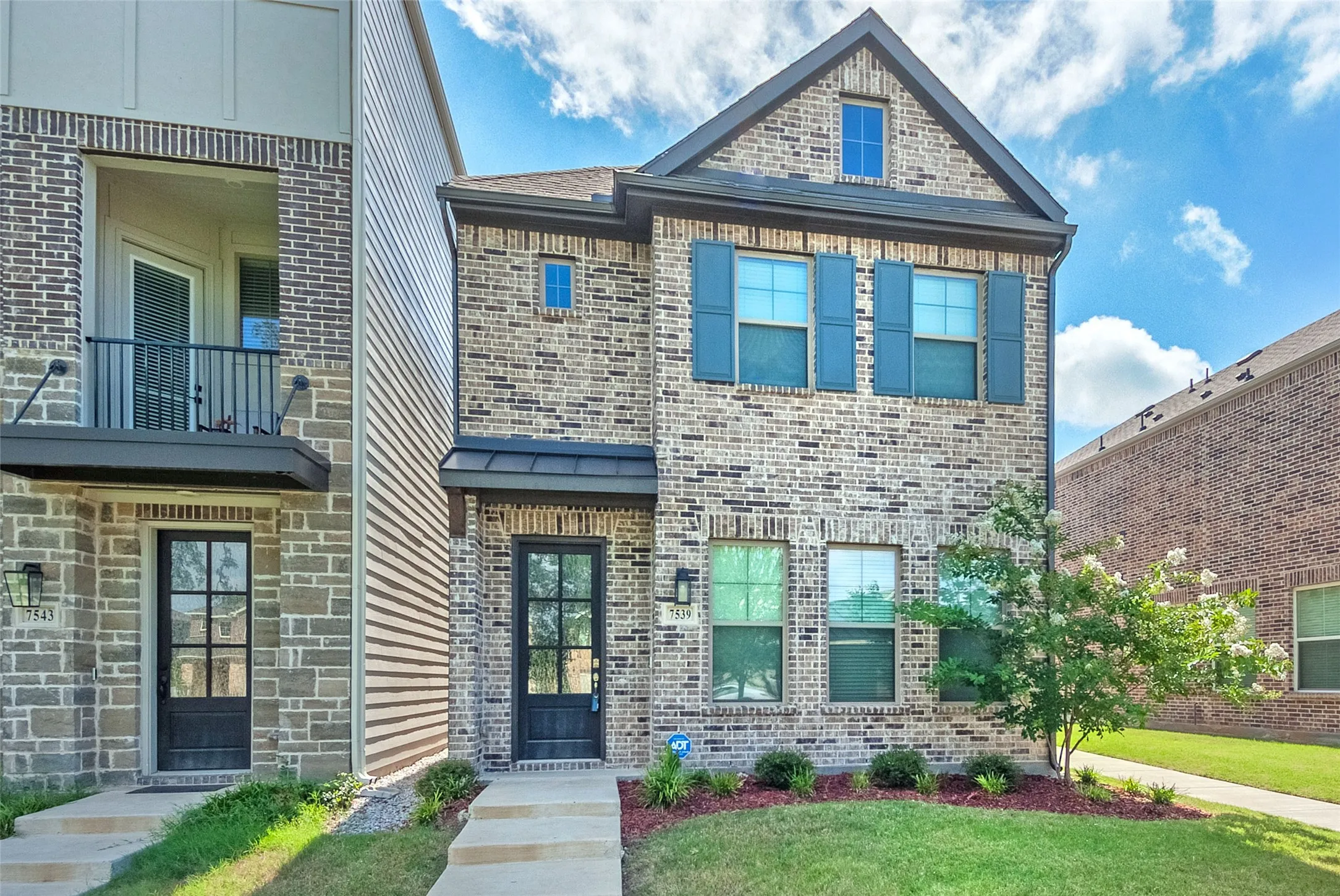 A charming two-story brick home with a well-kept front yard and vibrant greenery.