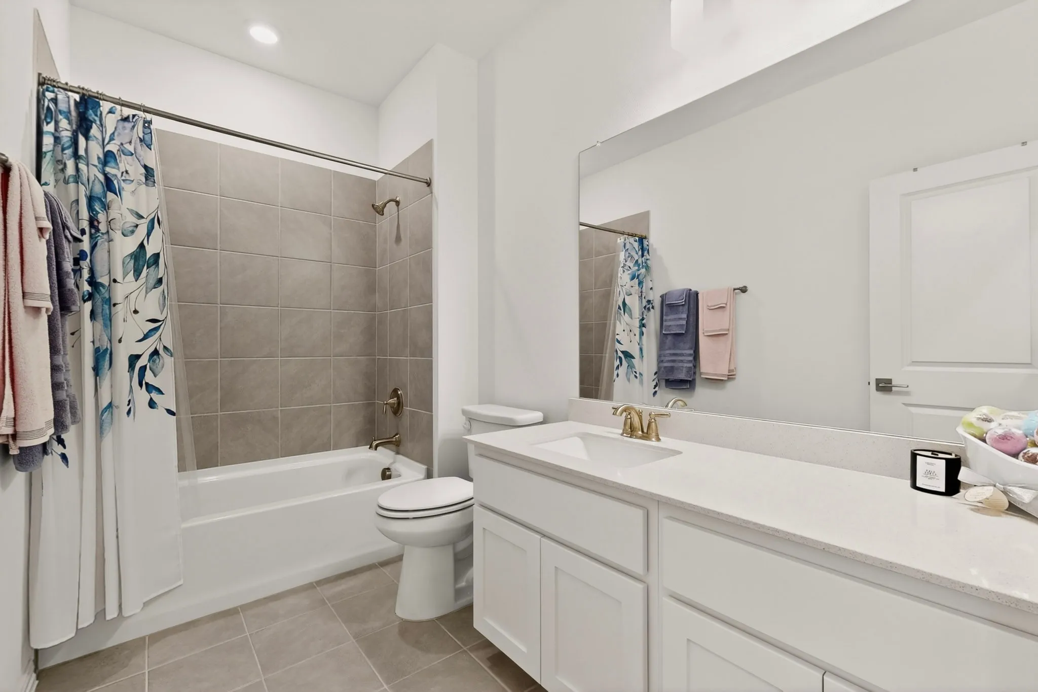 A bright bathroom with neutral-colored tiles featuring a bathtub, vanity, and a toilet.