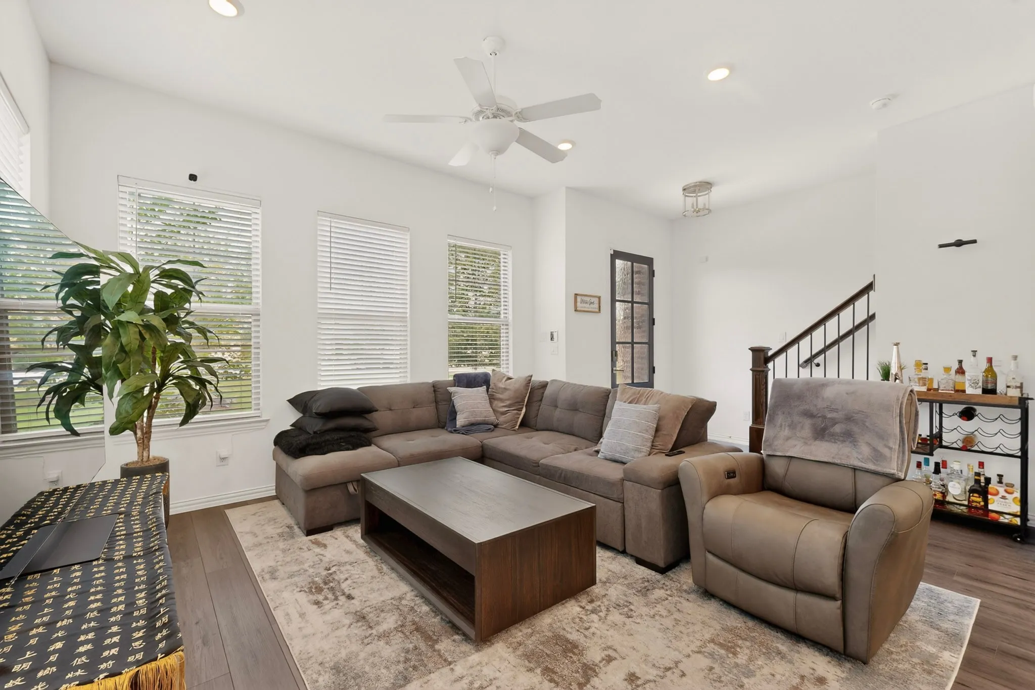 A cozy living room featuring hardwood floors, tall windows and a ceiling fan