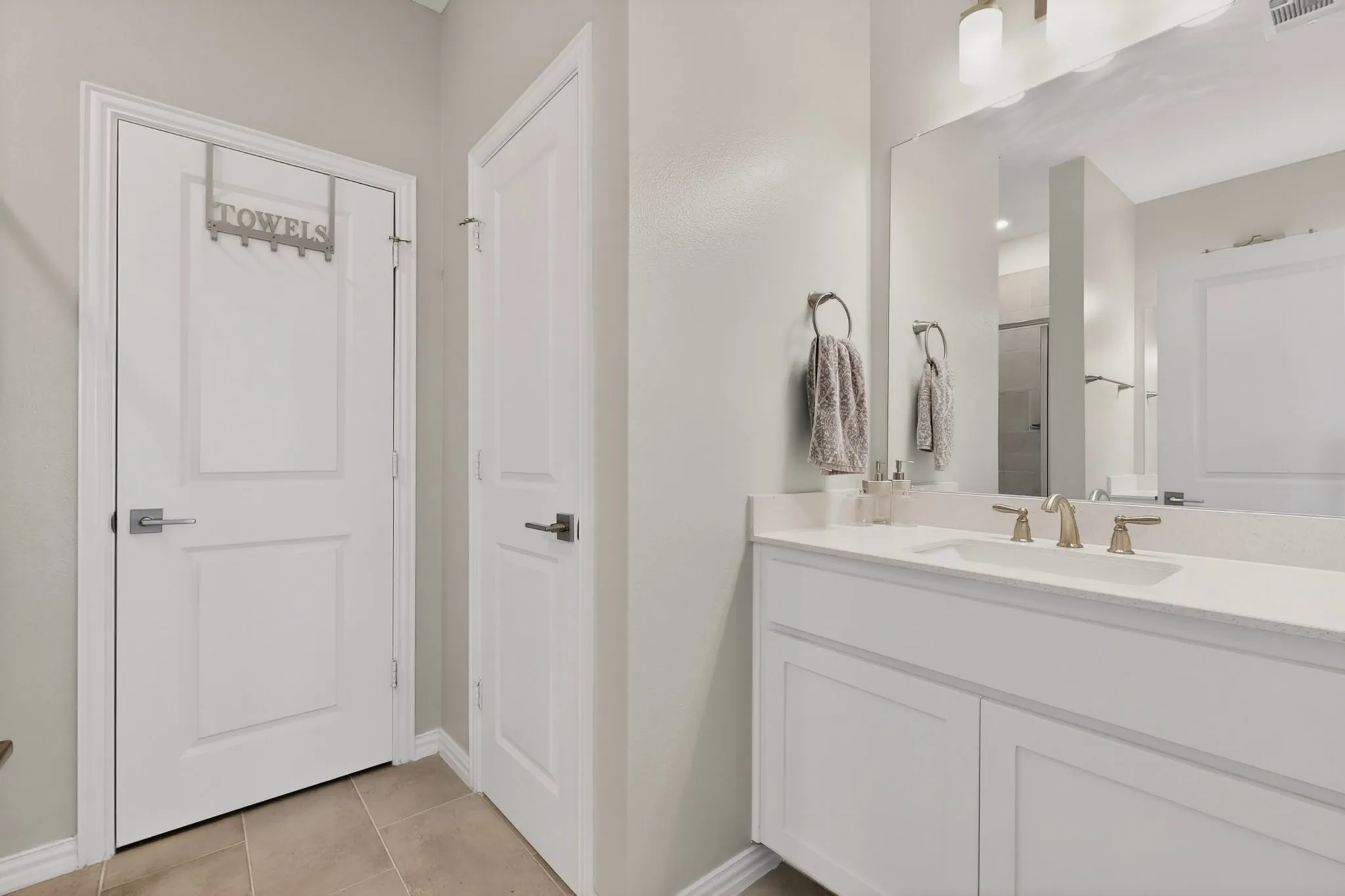 A bright primary bathroom featuring a vanity, linen closet and a separate room for the toilet