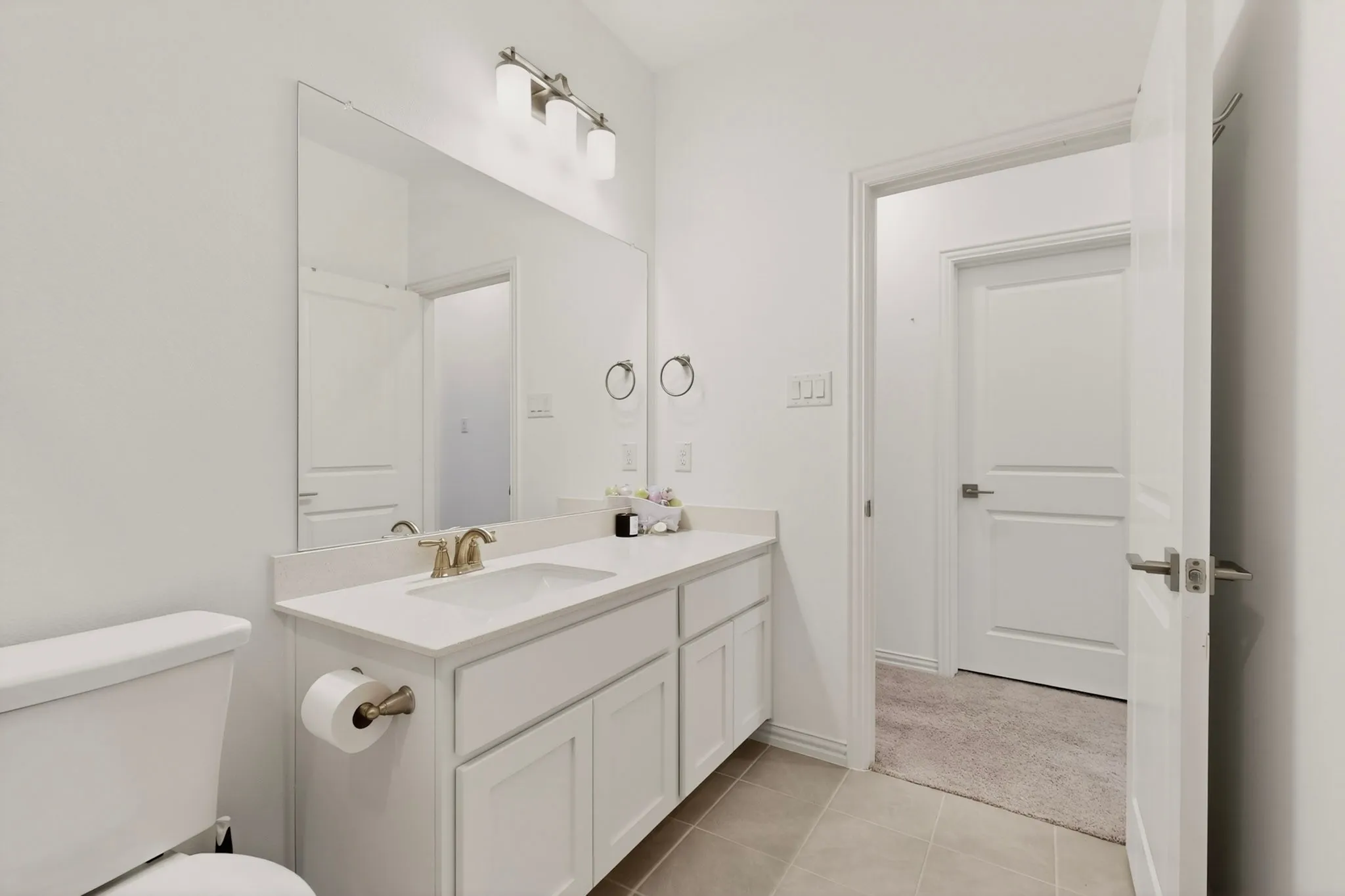 A bright bathroom with neutral-colored tiles featuring a vanity and a toilet.