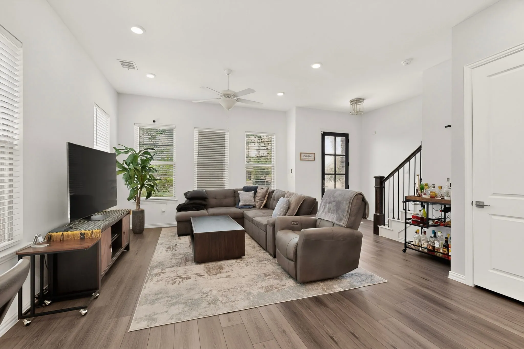 A cozy living room featuring hardwood floors, tall windows and a ceiling fan