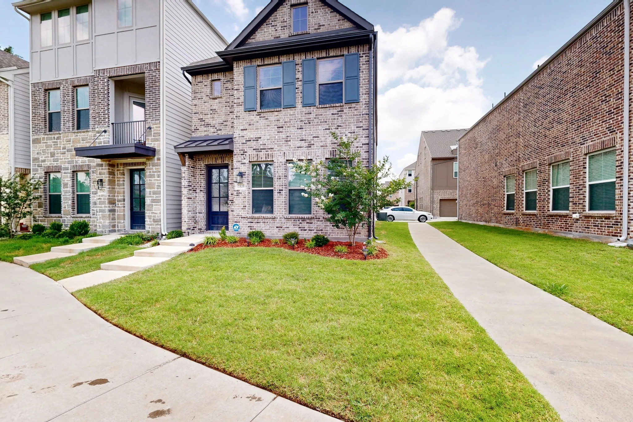 A charming two-story brick home with a lush green lawn, showcasing a welcoming suburban home environment.