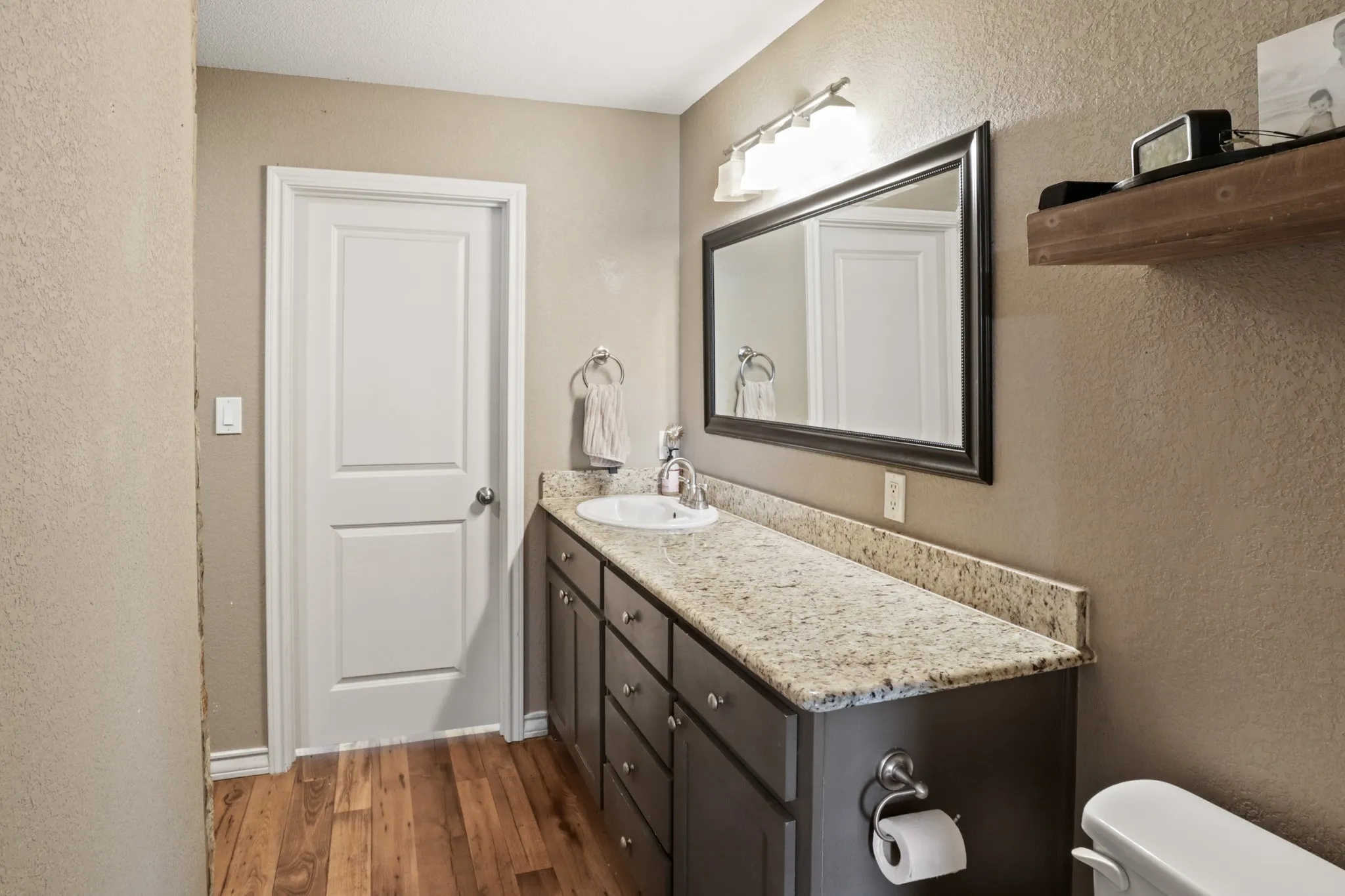 First Primary
Bathroom vanity featuring a light-colored granite countertop, an undermount sink, and a dark wood-finish cabinet with multiple drawers