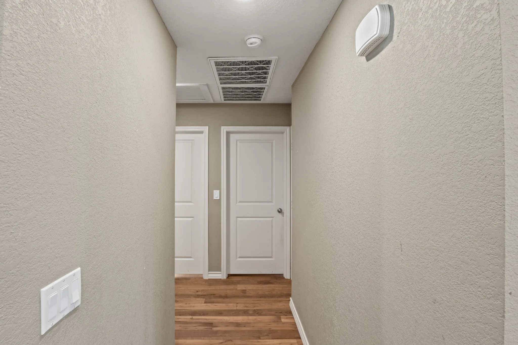 Interior hallway featuring neutral-toned textured walls, wood-finish flooring, and white paneled doors