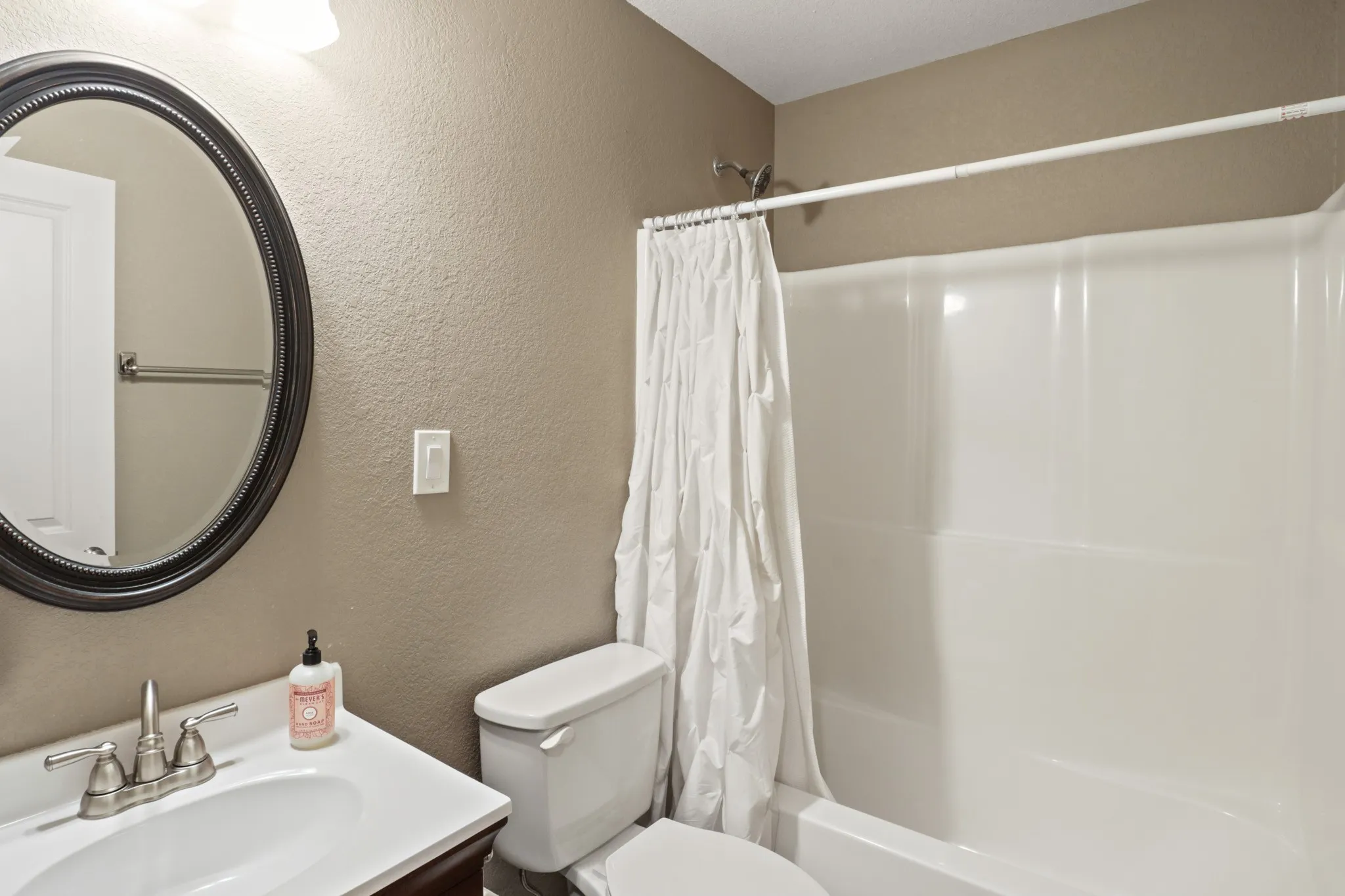 Hallway Bath White vanity with an integrated sink, brushed nickel faucet, and an oval framed mirror