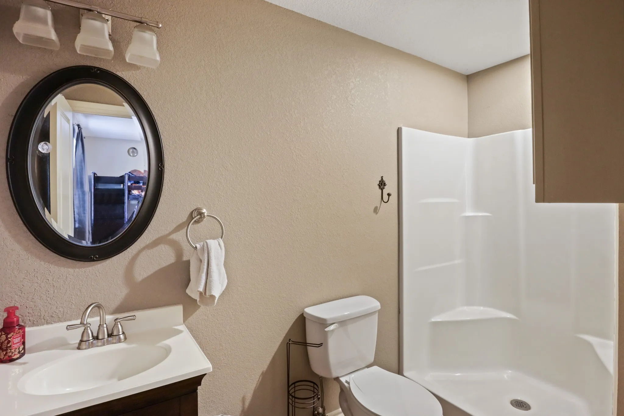 Second Primary Bathroom featuring a white integrated sink and countertop, dark wood vanity, oval mirror, and a white shower stall with built-in shelving