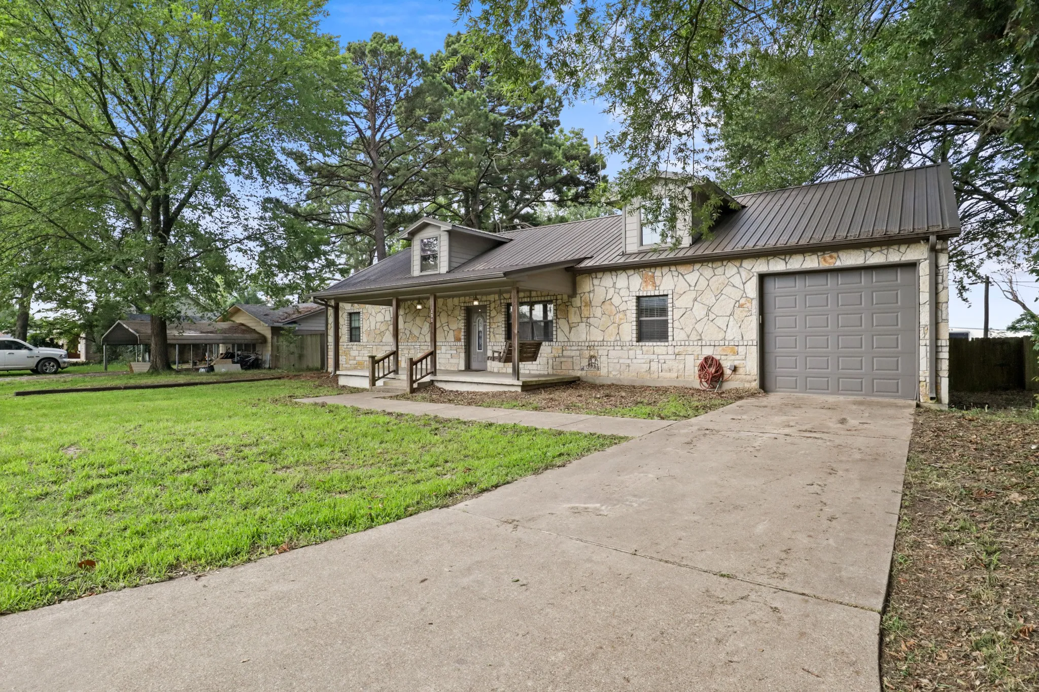 Stone veneer exterior featuring a covered porch with column supports, a metal roof, and an attached garage with a panel door