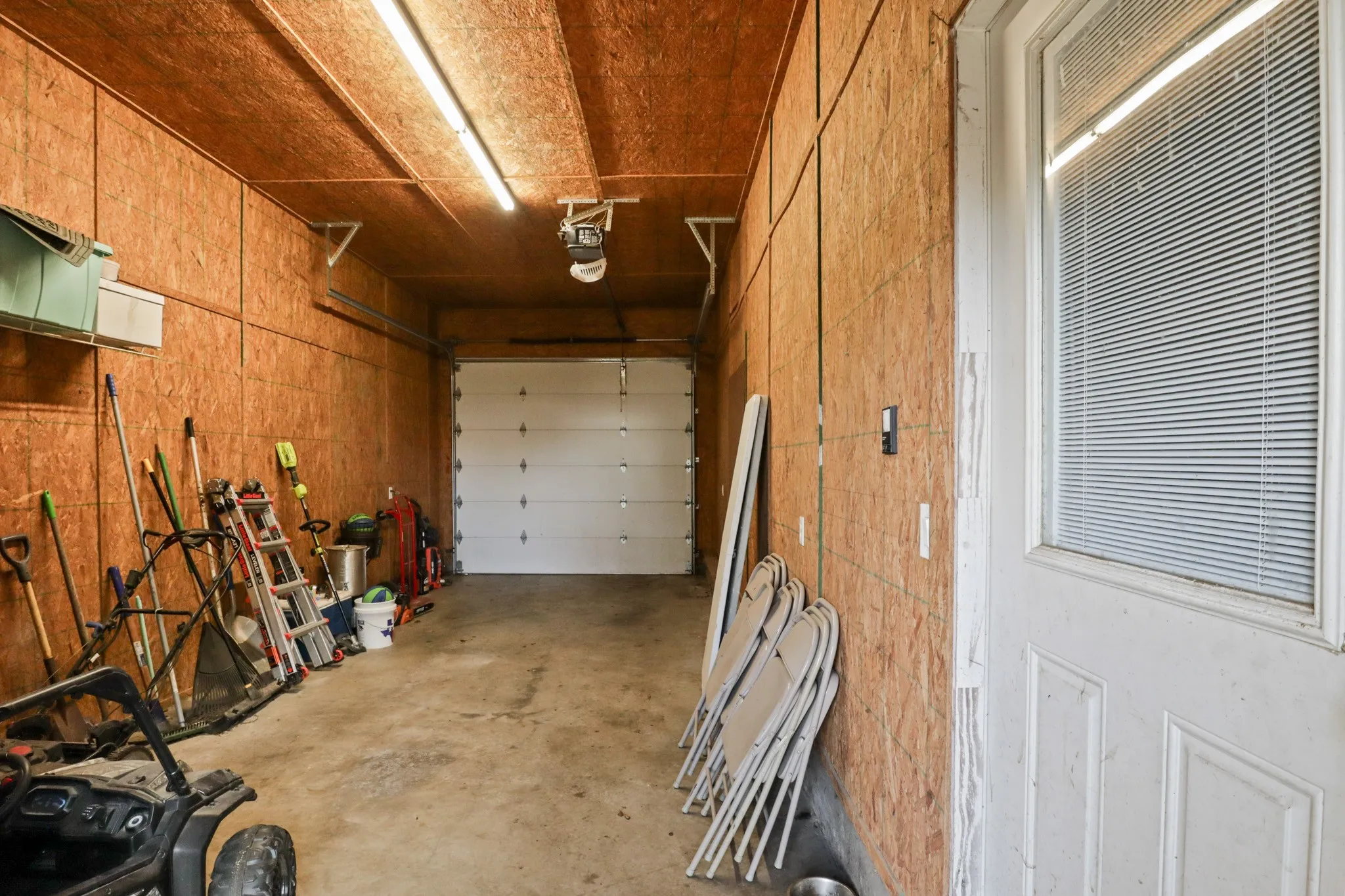 Garage space featuring a paneled overhead door, concrete flooring, and exposed wood-finish wall and ceiling panels