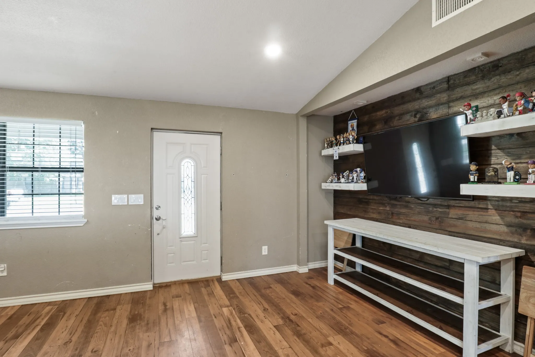 Expansive wood-finish flooring throughout the room, featuring a decorative front entry door with an arched glass insert