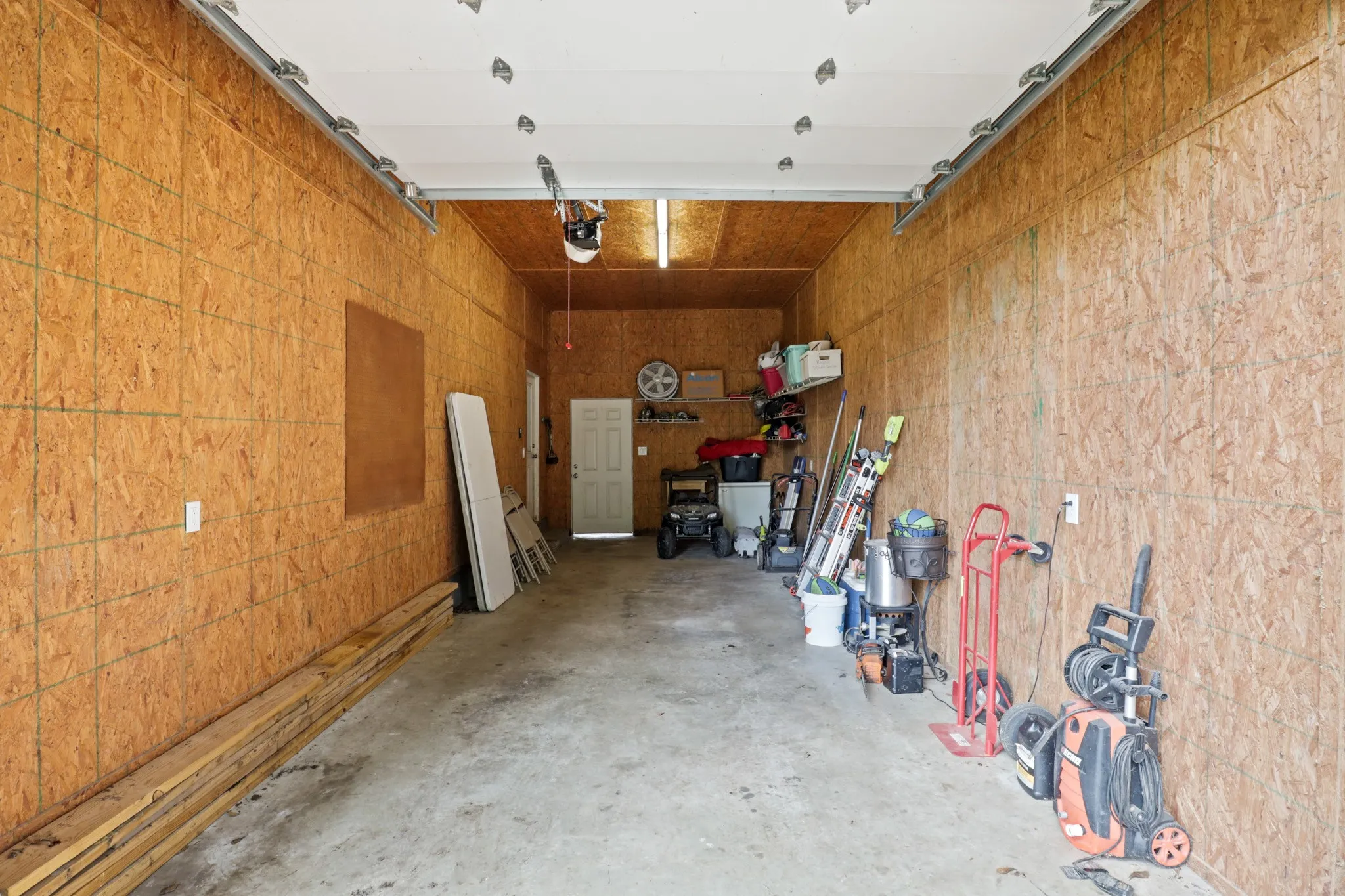 Spacious garage featuring composite wood paneling, concrete flooring, overhead lighting, and a white interior door