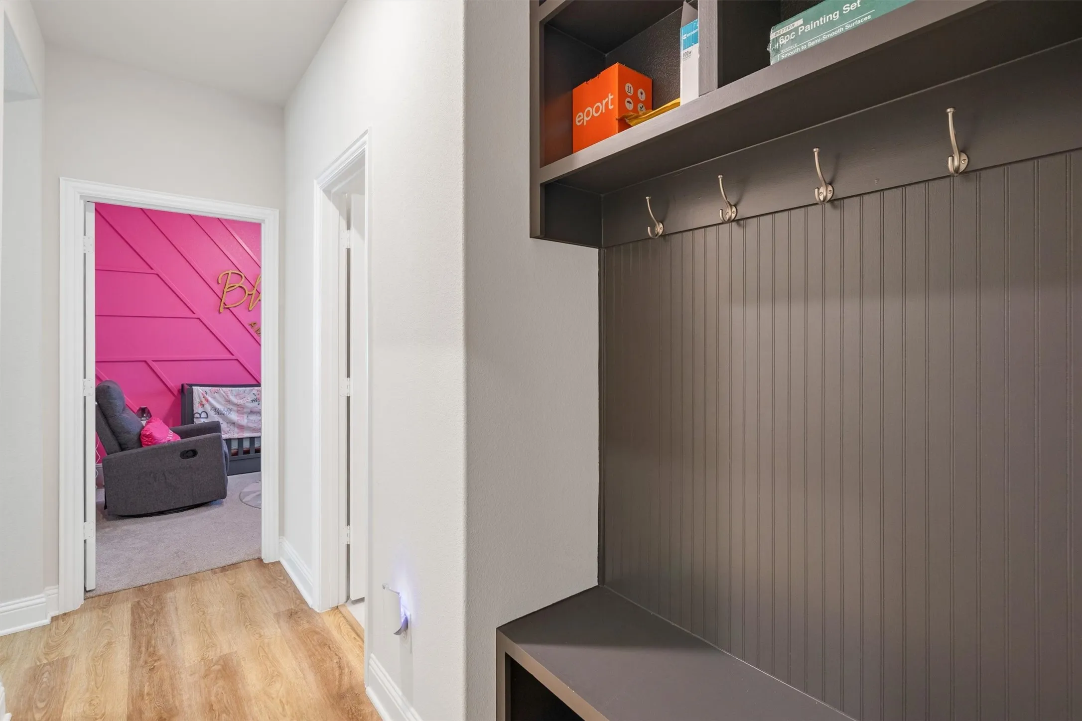Hallway featuring wood-finish flooring, white baseboards, and a built-in storage bench with beadboard paneling and coat hooks