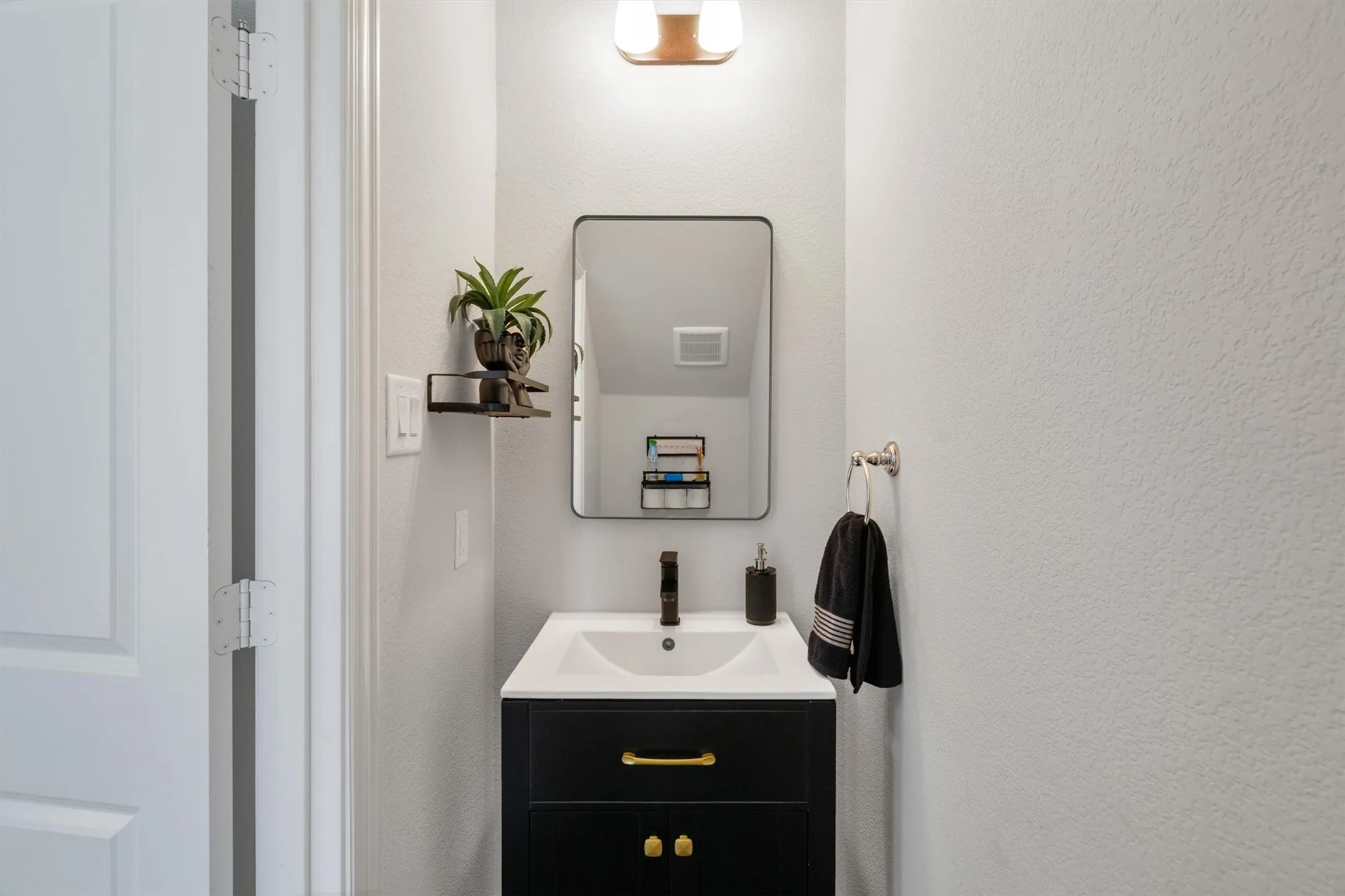 Modern vanity featuring a black cabinet with gold-tone hardware, a white integrated sink, and a black faucet