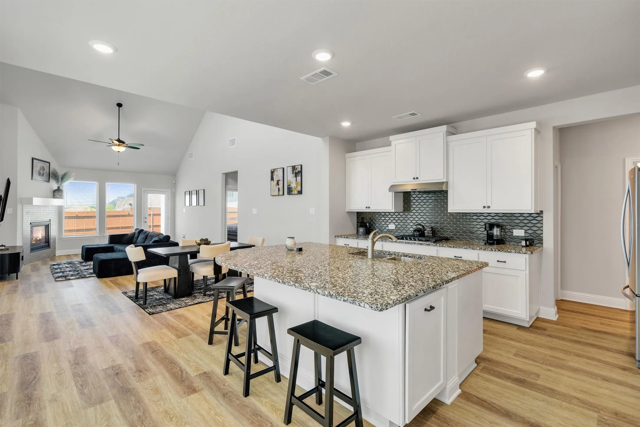Open-concept kitchen featuring an island with granite countertop, white cabinetry, and a textured tile backsplash