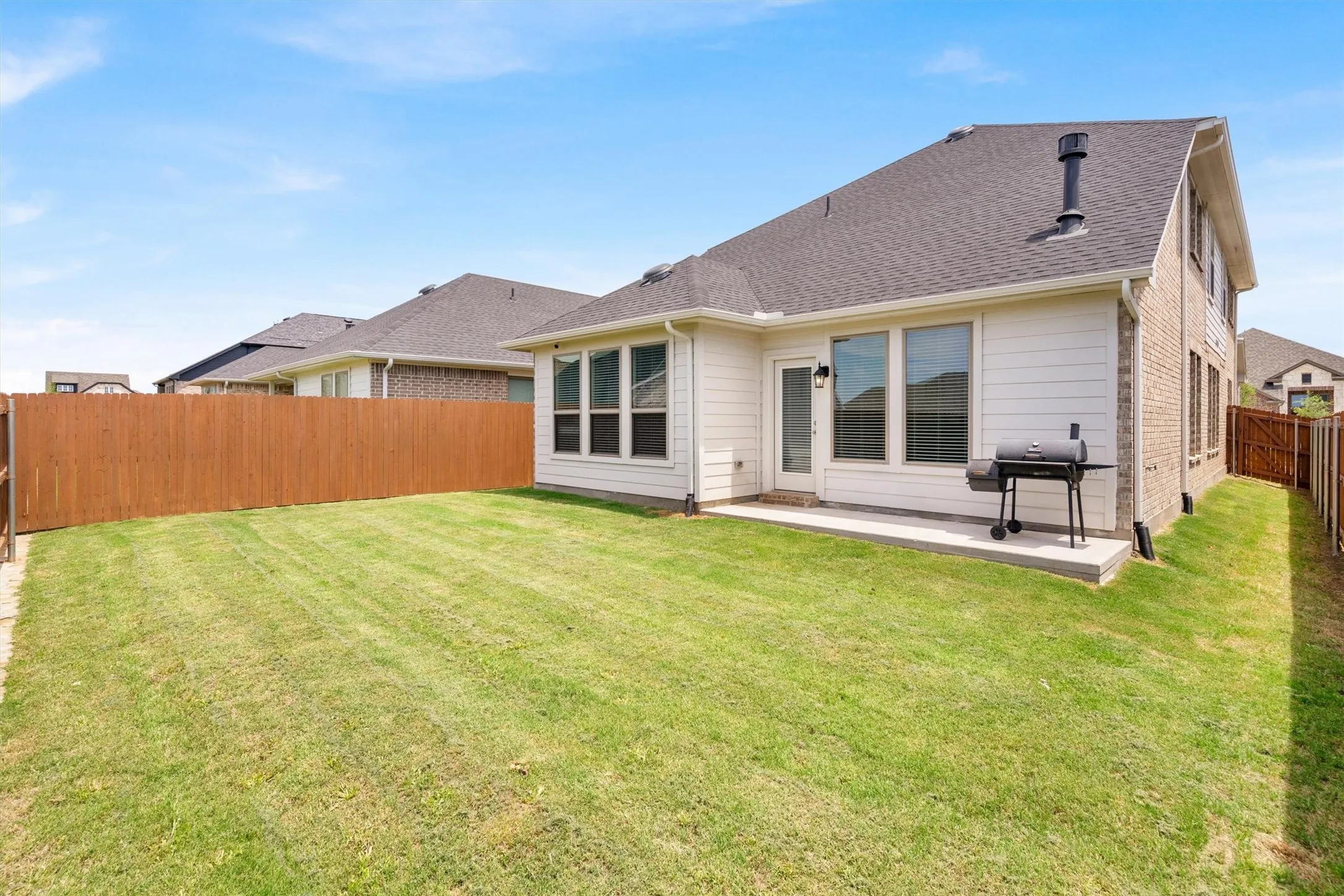 Expansive backyard featuring a manicured lawn, a full wood privacy fence, a concrete patio, a white paneled exterior, and a dark shingle roof
