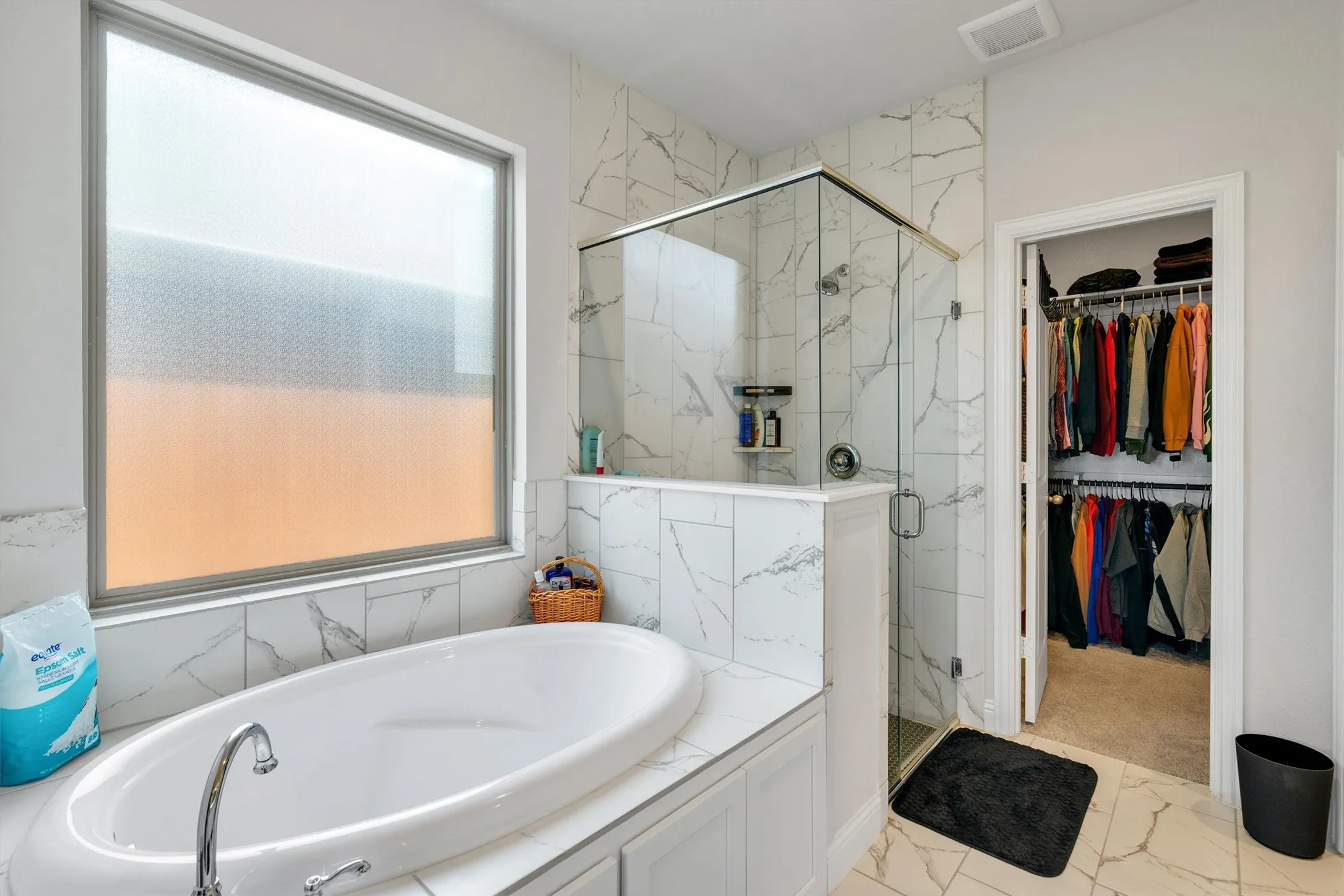 Freestanding oval soaking tub with chrome fixtures, surrounded by large format marble-look tile