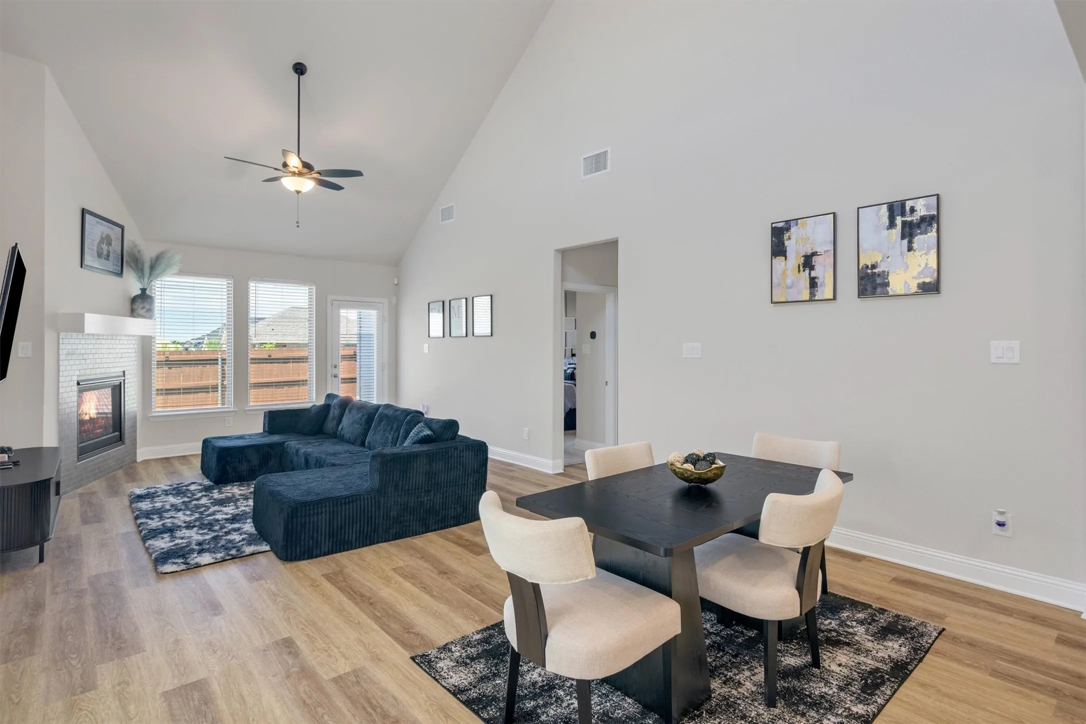 Vaulted ceilings enhance this open concept living space featuring wood-finish flooring, a contemporary fireplace with a tiled surround, and multiple windows