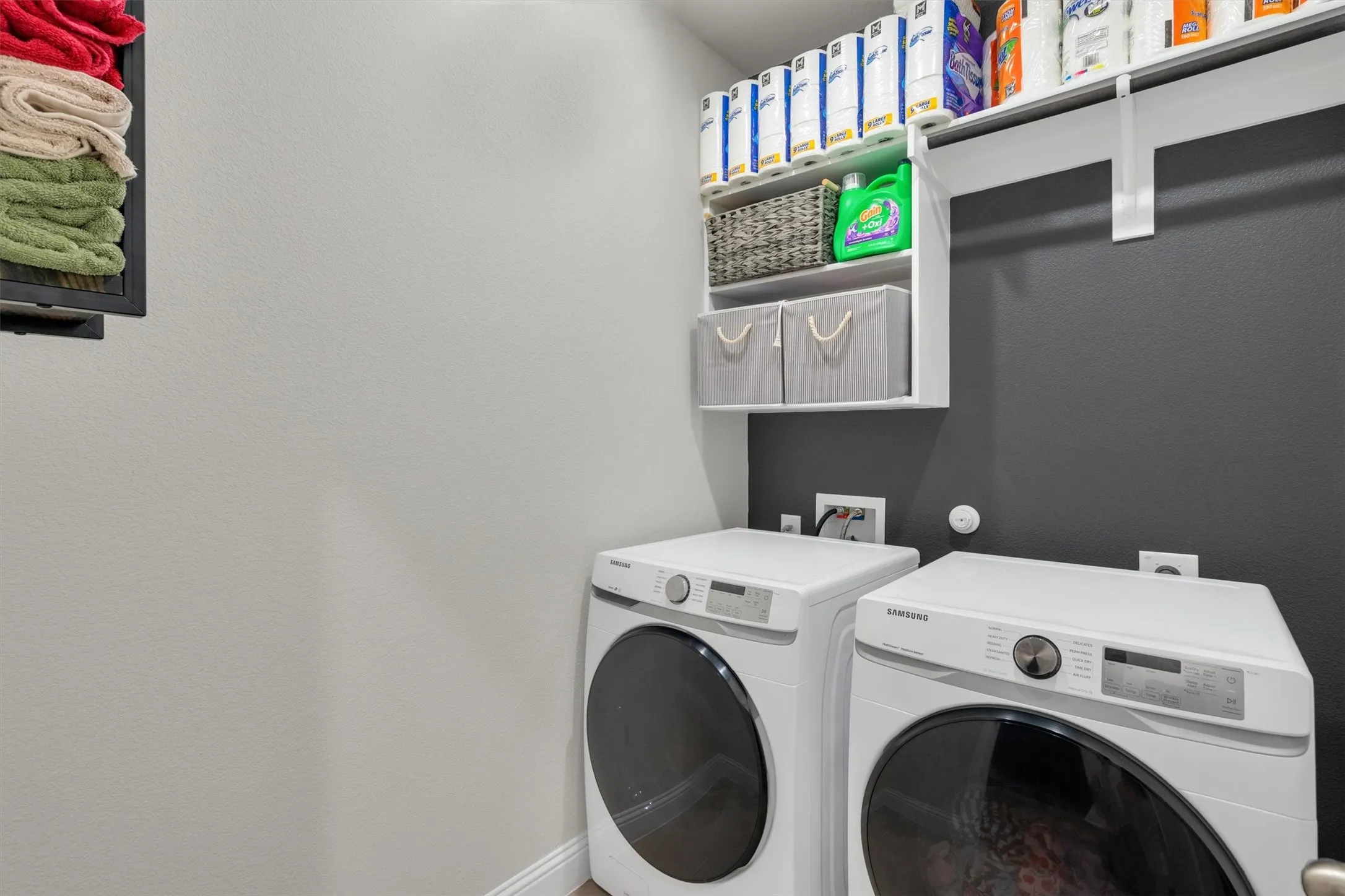 Dedicated laundry area featuring white washer and dryer units, overhead built-in shelving, and a dark accent wall