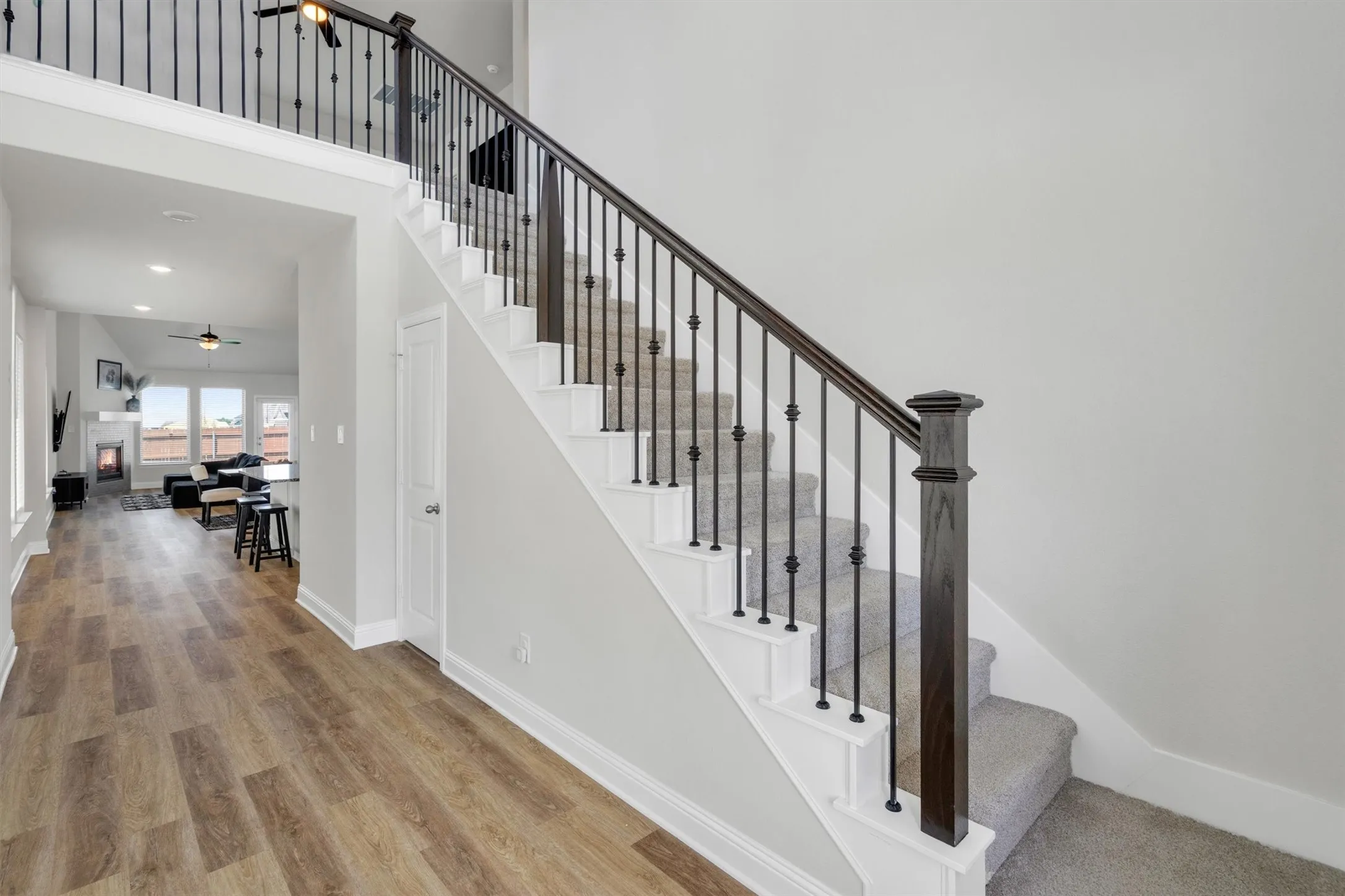 Staircase with dark wood handrails, black iron balusters, and light gray carpeted treads