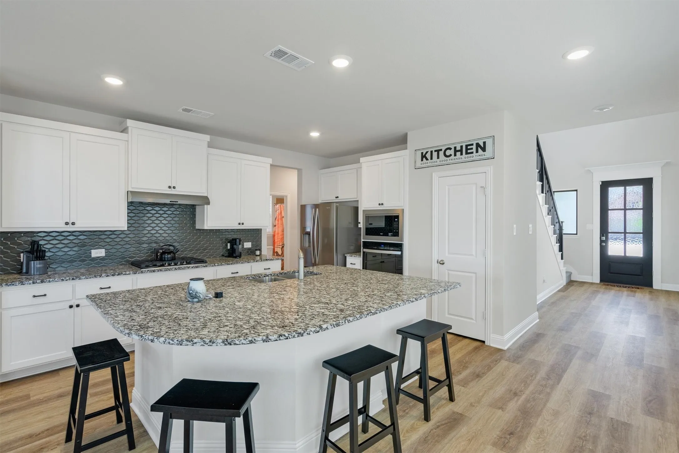 Contemporary kitchen featuring a large island with granite countertops, white cabinetry, a dark tile backsplash, stainless steel appliances, and wood-finish flooring