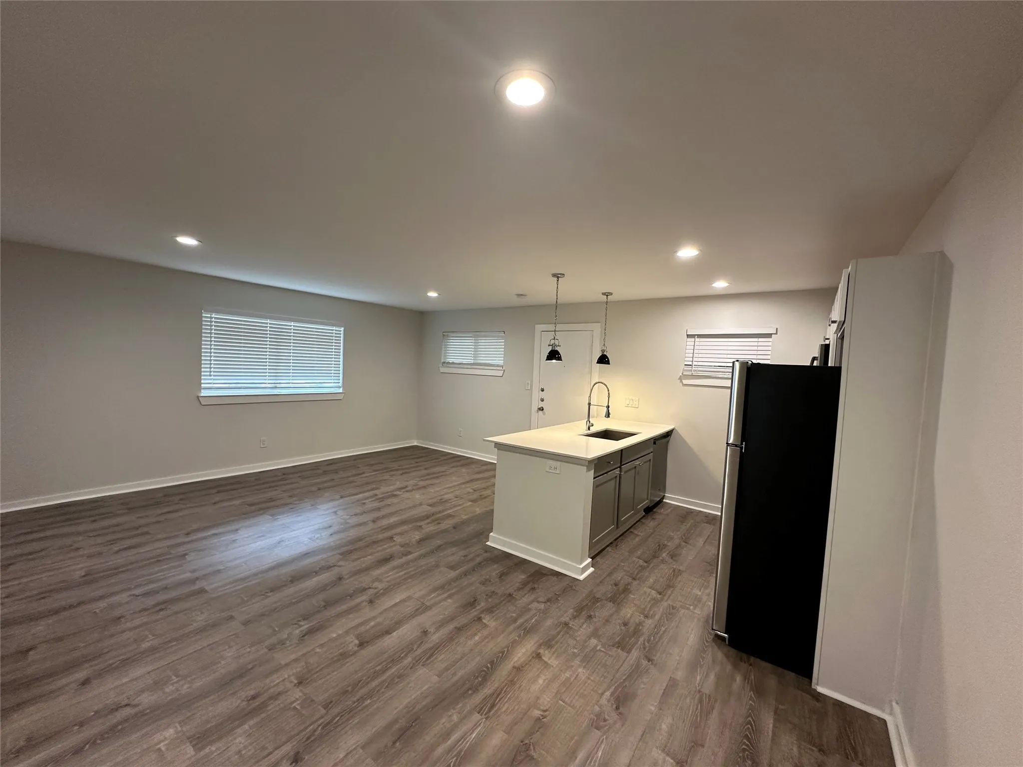 Open-concept living space featuring wood-finish flooring, recessed lighting, and a kitchen island with a built-in sink and pendant lighting