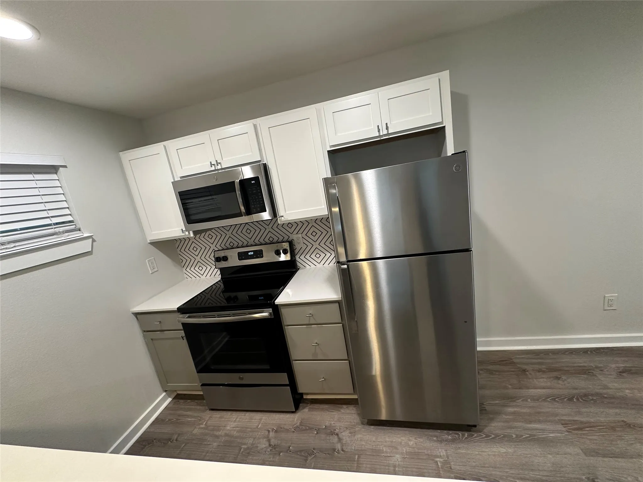 Kitchen featuring stainless steel appliances, white upper cabinetry, gray lower cabinetry, a patterned tile backsplash, and wood-finish flooring