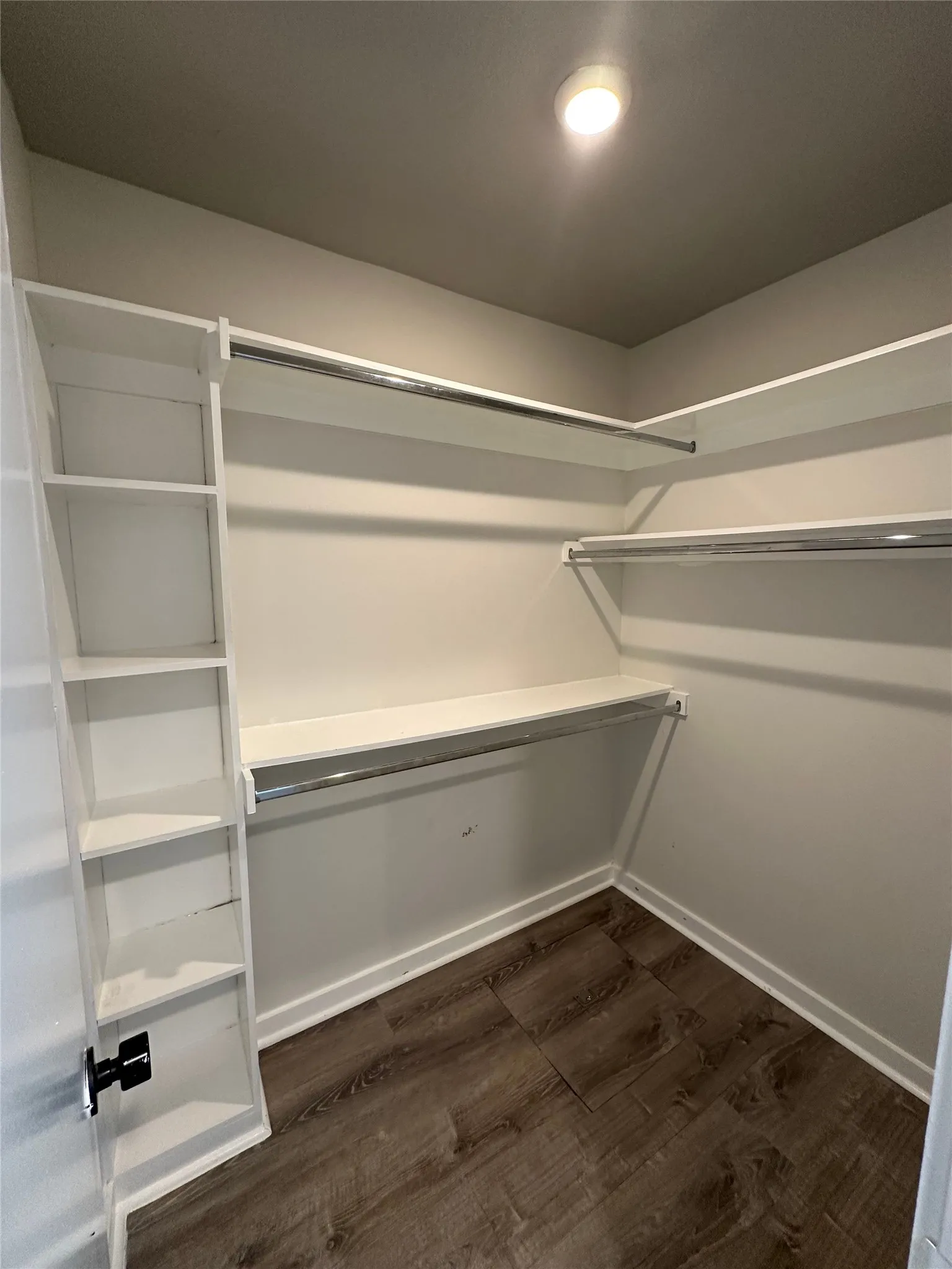Walk-in closet featuring wood-finish flooring, recessed lighting, white built-in shelving, white baseboards, and chrome hanging rods